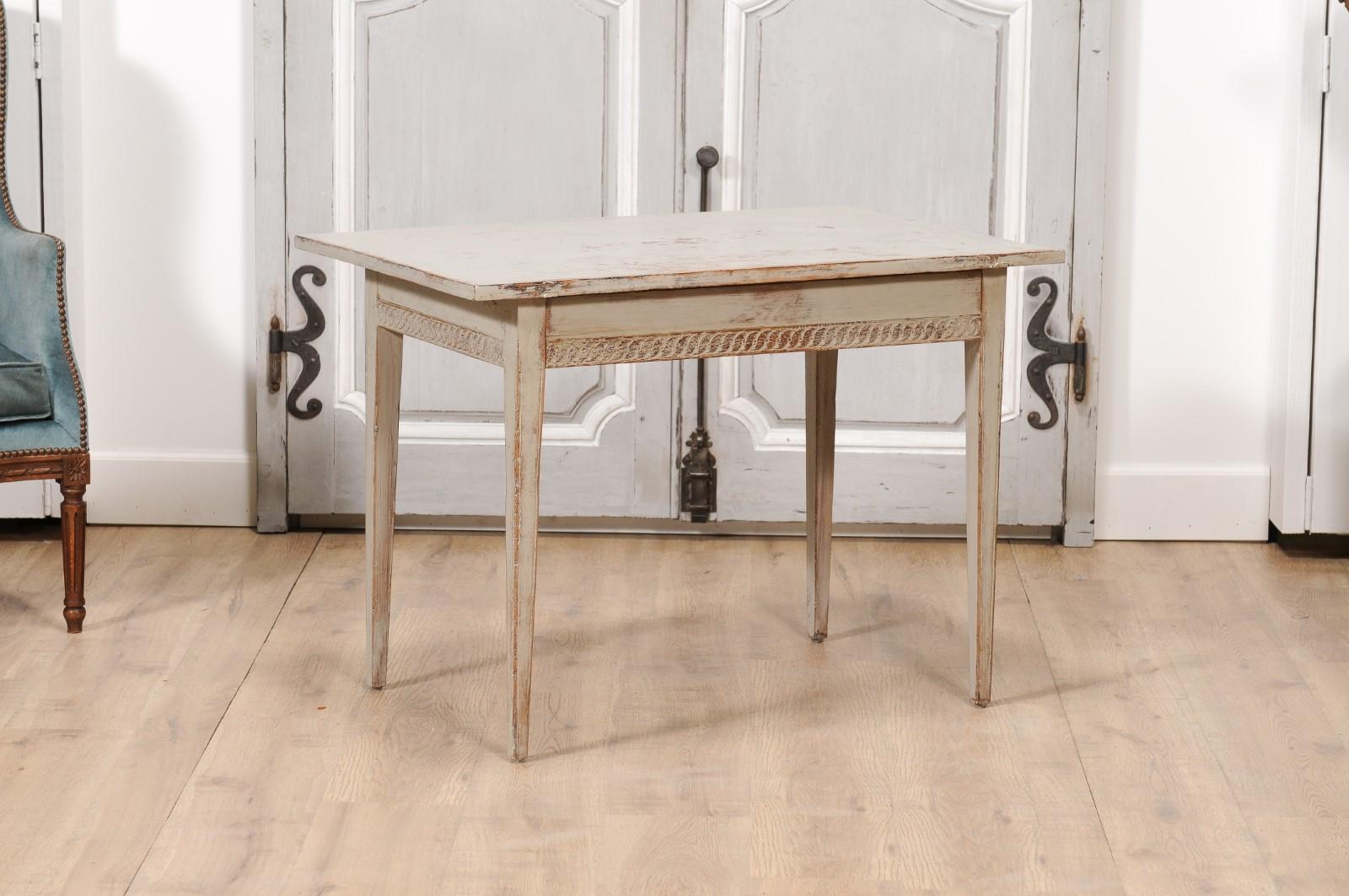 A Swedish Gustavian period painted wood side table from circa 1790 with carved guilloches on the apron, distressed finish and tapered legs. Immerse yourself in the pure, unadulterated elegance of Swedish Gustavian design with this painted wood side