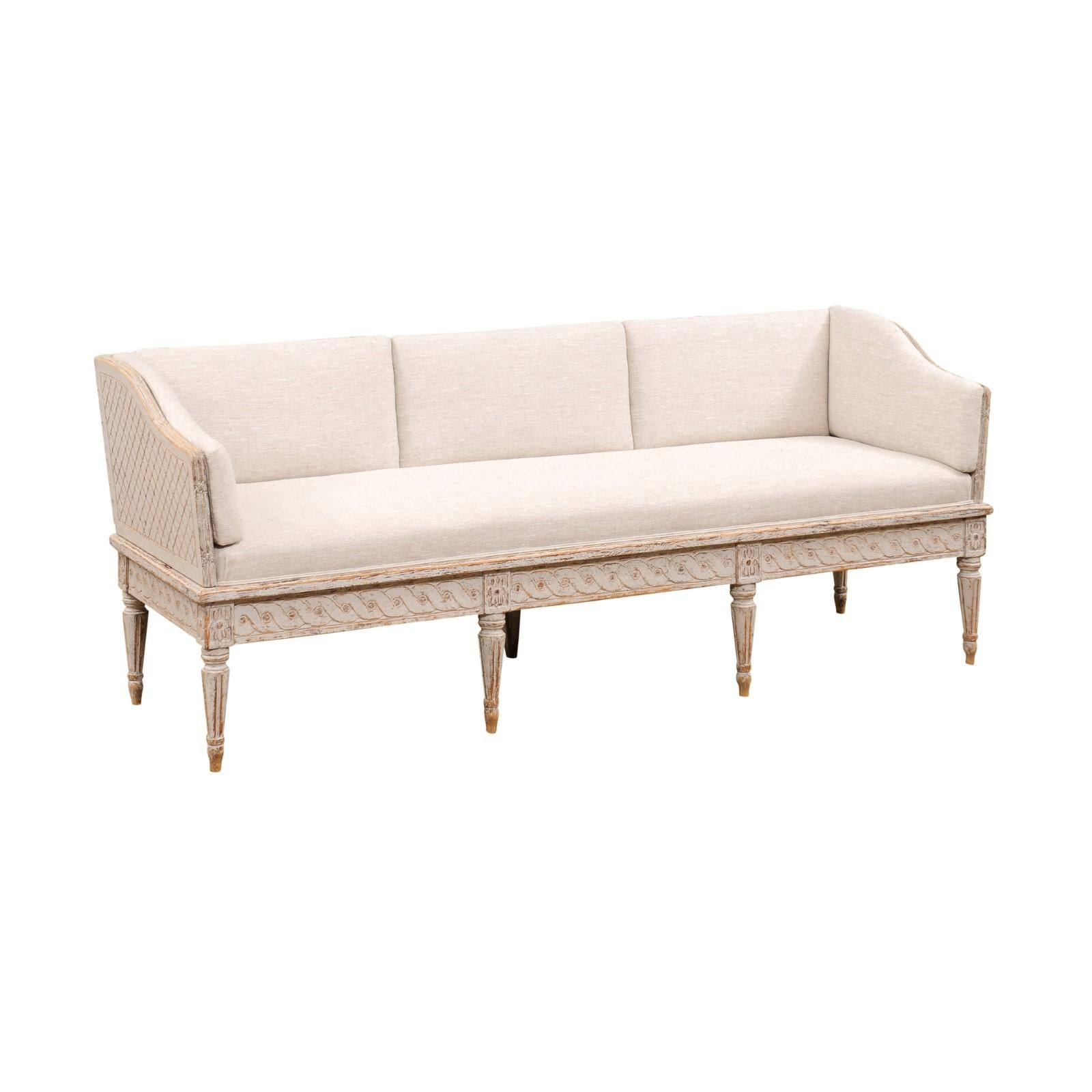 A Swedish Gustavian period painted wood Trågsoffa from the late 18th century, with upholstered seat, carved guilloche frieze, cross-hatched sides and fluted legs. Created in Sweden during the last quarter of the 18th century, this Gustavian period