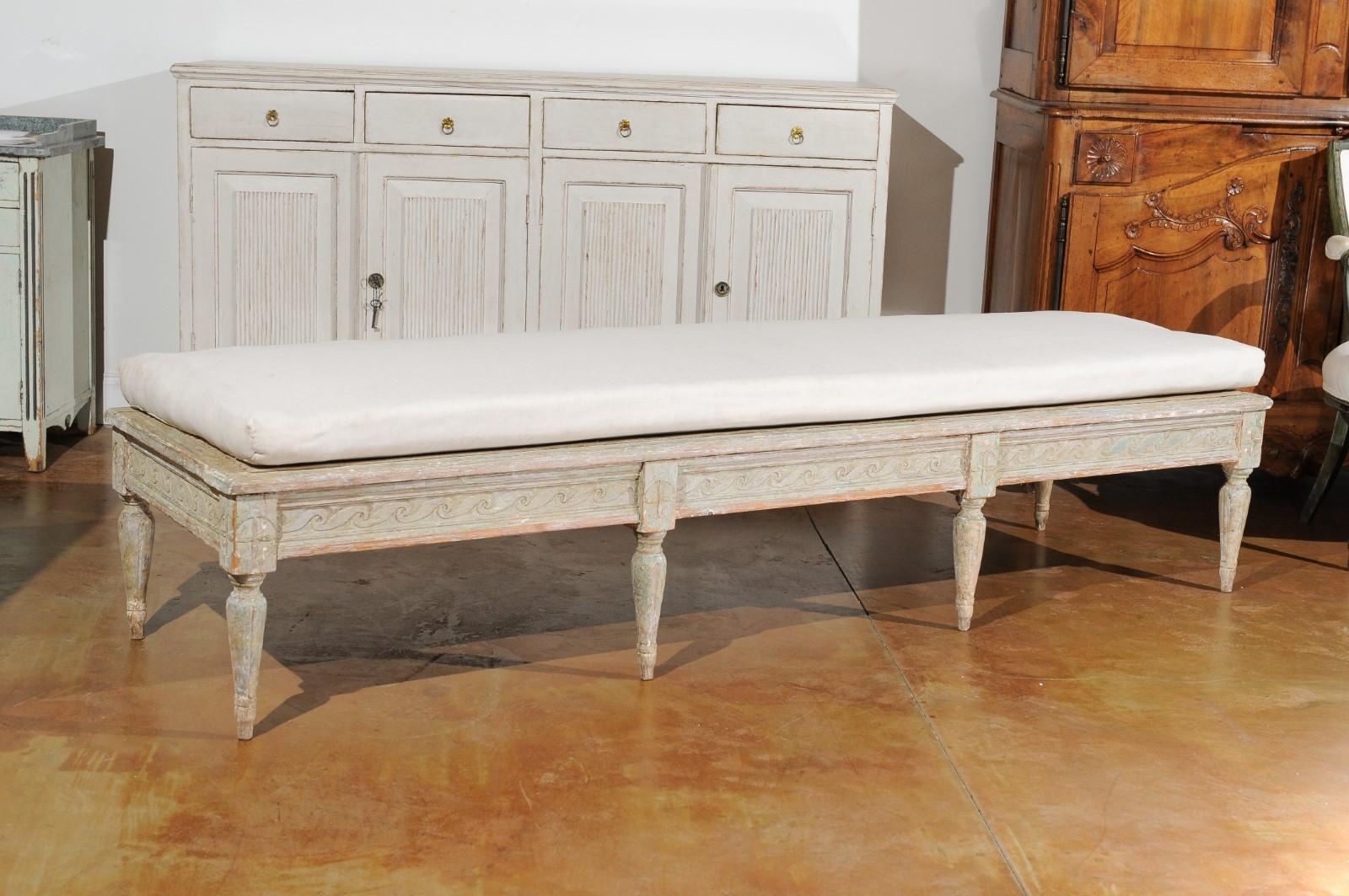 A Swedish Gustavian period painted wood bench from the late 18th century, with Vitruvian scroll frieze and distressed patina. Created in Sweden during the last decade of the 18th century, this Gustavian bench features a long upholstered seat,