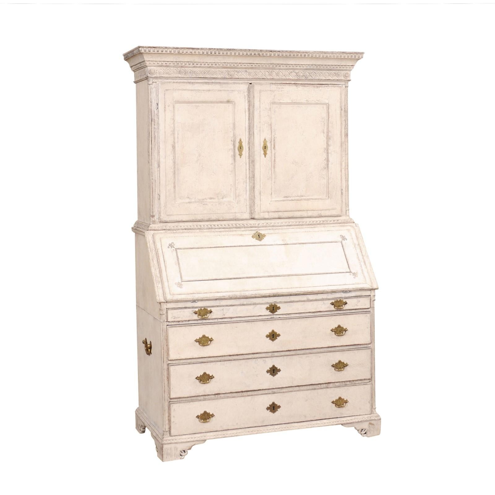 A Swedish Gustavian period two-part tall secretary from circa 1790 with elegant carved décor, creamy white painted finish and multiple inner drawers inside the slant-front desk. Discover the understated elegance of this Swedish Gustavian period tall