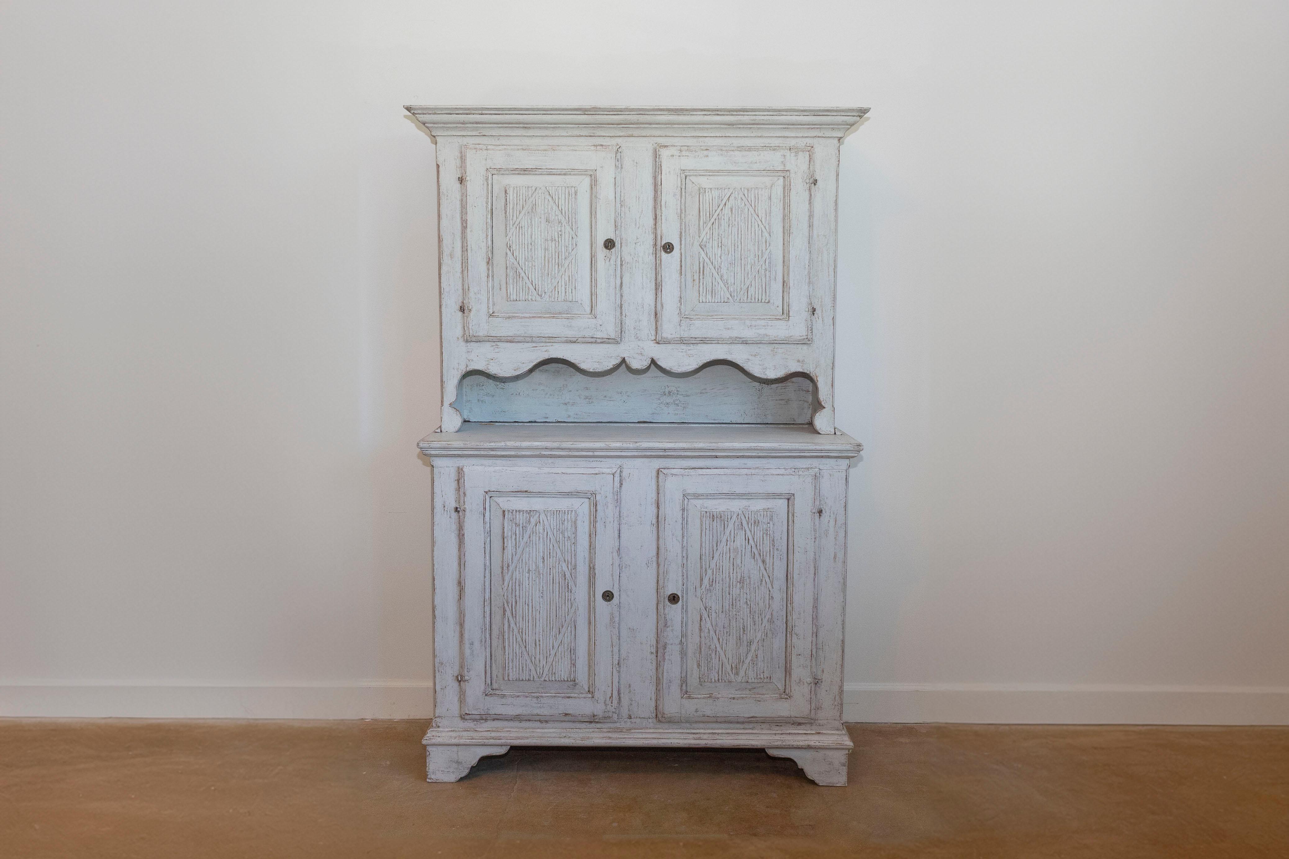 A Swedish Gustavian period two-part wooden cabinet from the early 19th century, with diamond motifs, four doors, carved open shelf and distressed patina. Created in Sweden during the early years of the 19th century, this wooden cabinet features a