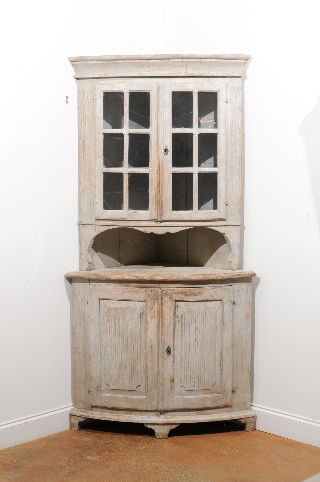 A Swedish Gustavian period painted corner cabinet from the early 19th century with glass doors, open shelf, reeded motifs and nicely distressed patina. Created in Sweden during the early years of the 19th century, this Swedish corner cabinet