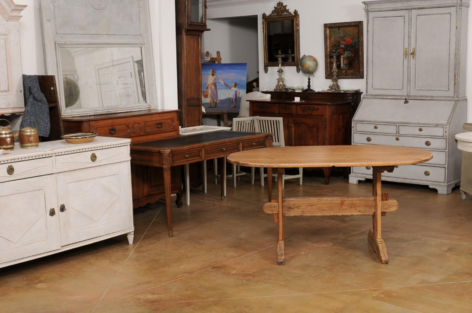 A Swedish Gustavian period rustic dining room table from the early 19th century, with oval top, trestle base and distressed patina. Created in Sweden during the early years of the 19h century, this Gustavian period dining room table charms us with