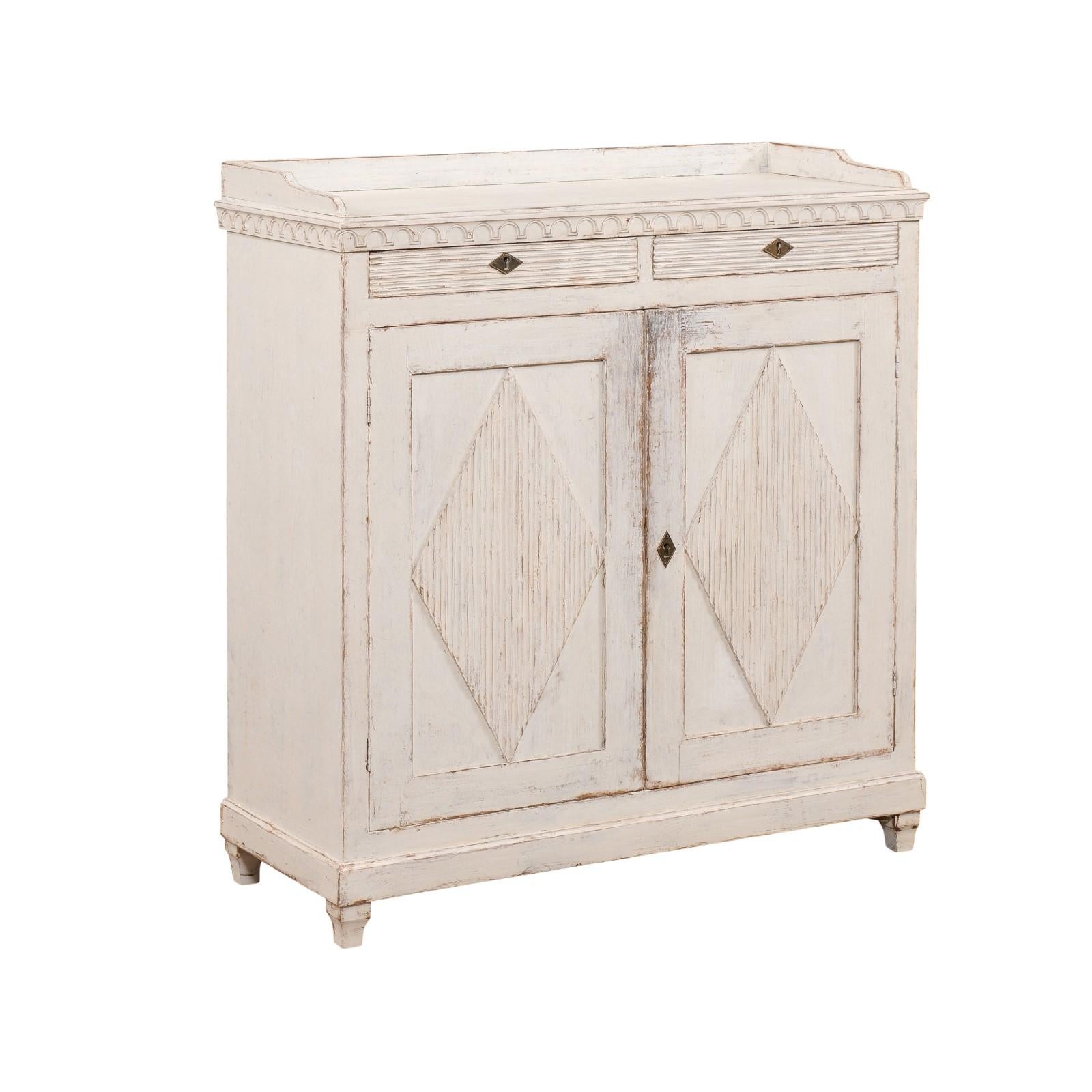 A Swedish Gustavian period painted wood sideboard from the early 19th century, with three-quarter gallery, carved frieze, two drawers, two doors and reeded diamond motifs. Created in Sweden during the early years of the 19th century, this painted