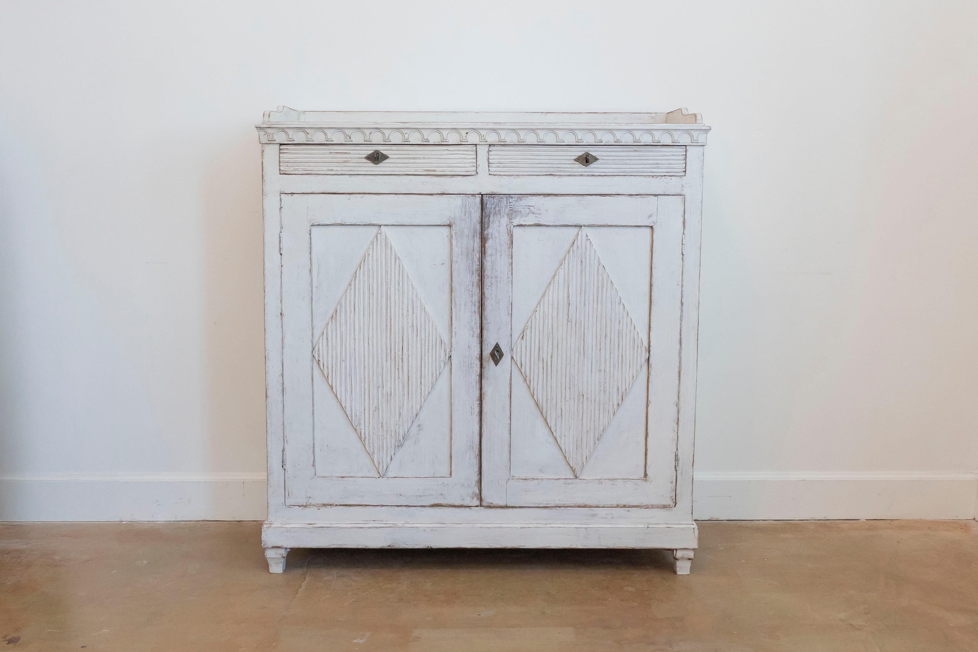Aparador sueco de madera pintada de la época Gustaviana, de principios del siglo XIX, con galería de tres cuartos, friso tallado, dos cajones, dos puertas y motivos de rombos acanalados. Creado en Suecia durante los primeros años del siglo XIX, este