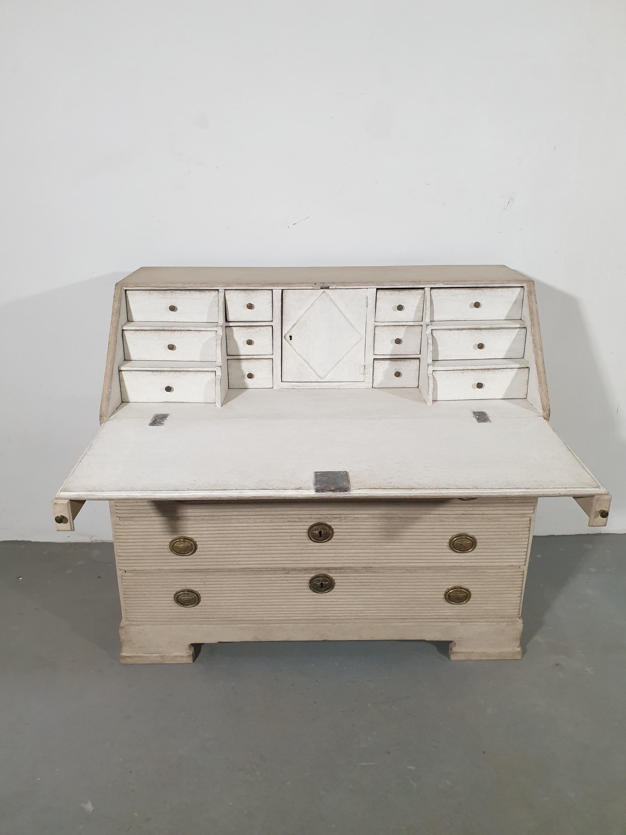 A Swedish Late Gustavian period secretary from circa 1820, with tan/cream painted finish, slant-front desk, five drawers, carved reeded motifs and bracket feet. Embrace the timeless elegance of the Swedish Late Gustavian period with this exquisite