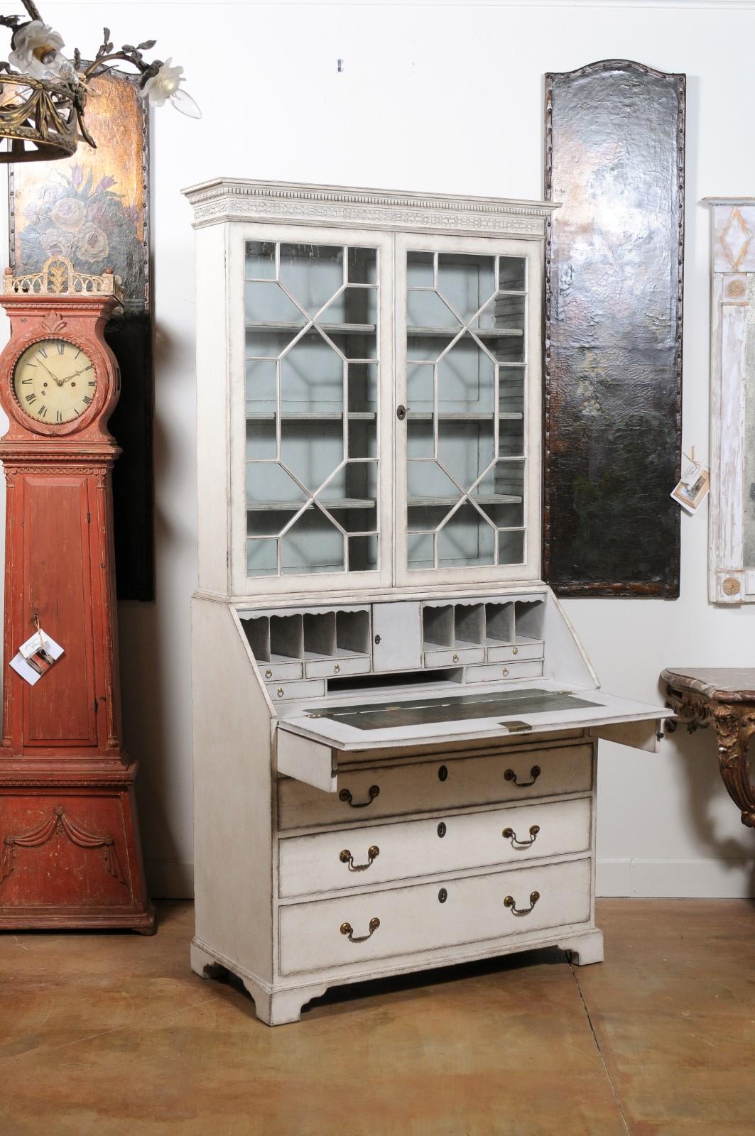 A Swedish painted vitrine secretaire from the early 19th century, with slant front desk and mullioned glass doors. Created in Sweden during the first quarter of the 19th century, this secretaire features a carved cornice with dentil molding and