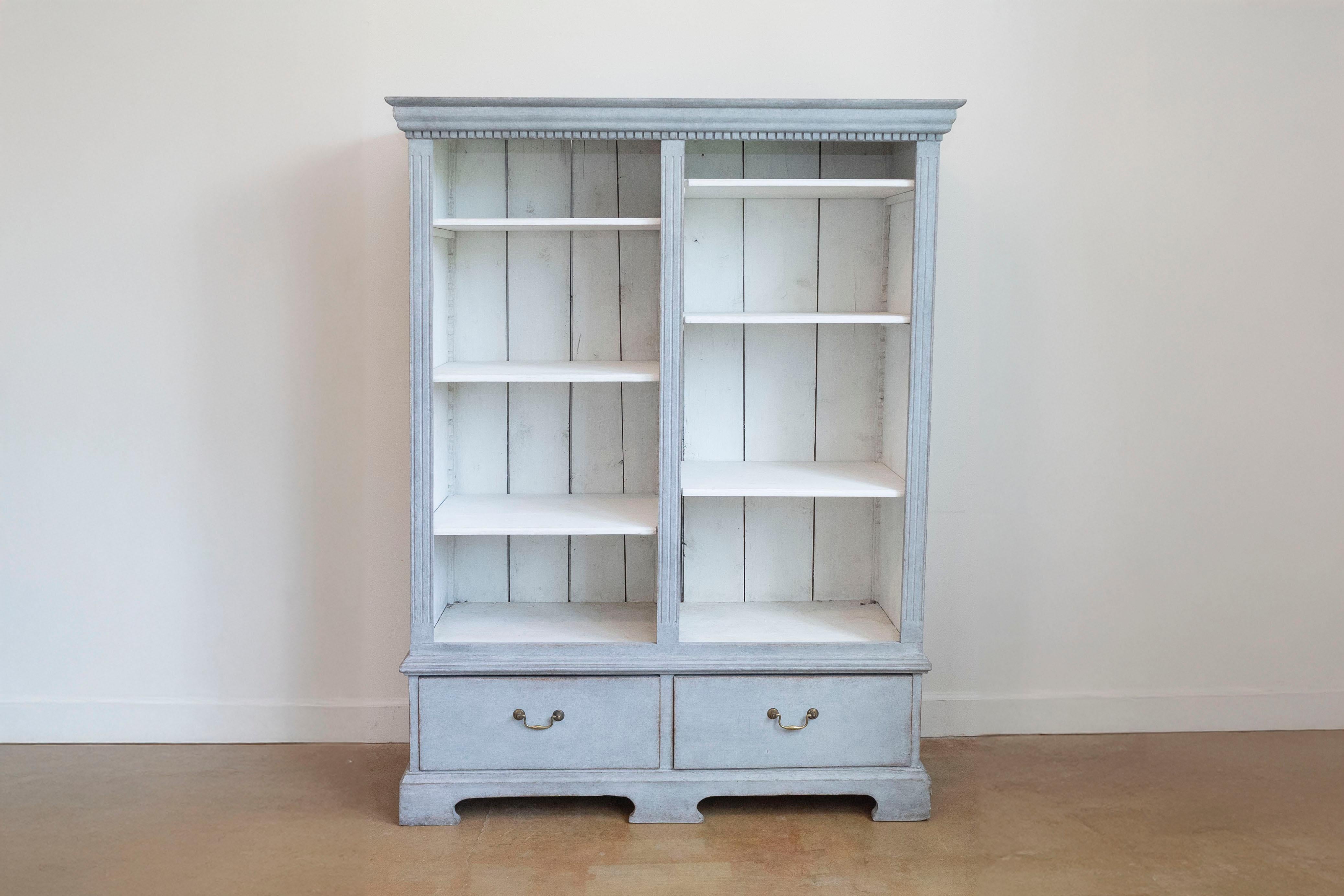Ein schwedisches Bücherregal aus Holz um 1850 mit grauem Anstrich, geschnitzter Zinnenleiste, offenen Regalen, zwei Schubladen und Klammerfüßen. Dieses schwedische Holzregal aus der Zeit um 1850 ist ein Zeugnis für die zeitlose Anziehungskraft