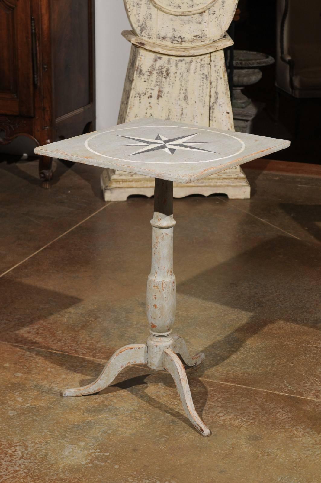 A Swedish grey painted guéridon side table with pedestal base and star motifs from the mid-19th century. This Swedish painted side table features an almost square top, adorned with an exquisite wind rose motif. This top is raised on a turned
