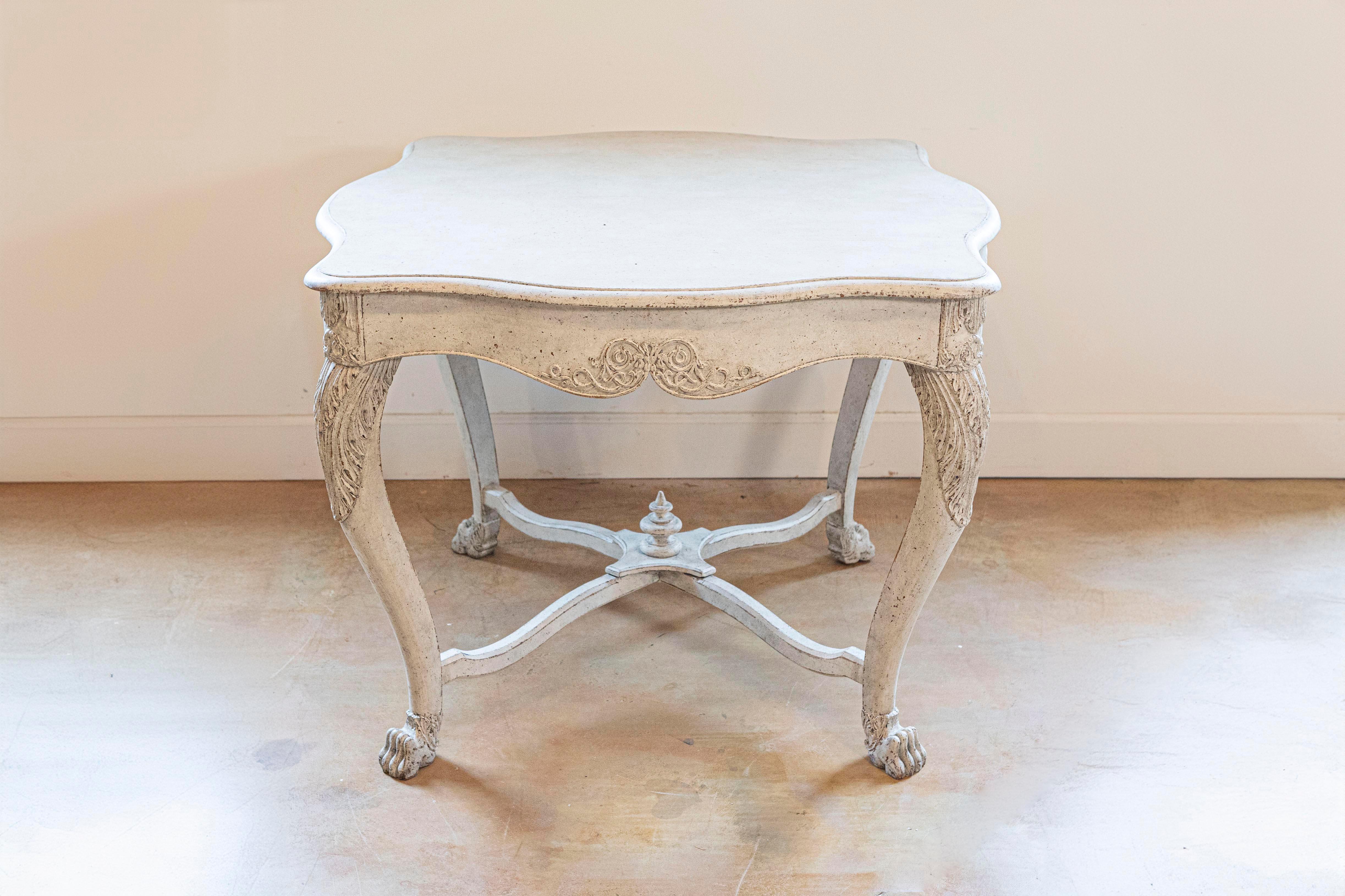 Table centrale suédoise peinte du milieu du XIXe siècle, avec des motifs sculptés et une traverse. Créée en Suède dans les années 1850, cette table peinte présente un plateau presque carré aux lignes serpentines, surmontant un tablier sculpté de