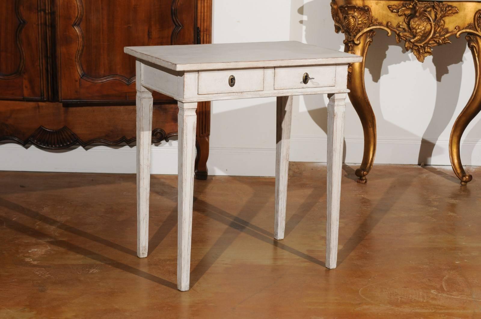 A Swedish Gustavian style painted side table from the mid-19th century, with two drawers and tapered legs. This elegant Swedish side table features a rectangular top, sitting above two small drawers, each fitted with an oval escutcheon. The table is