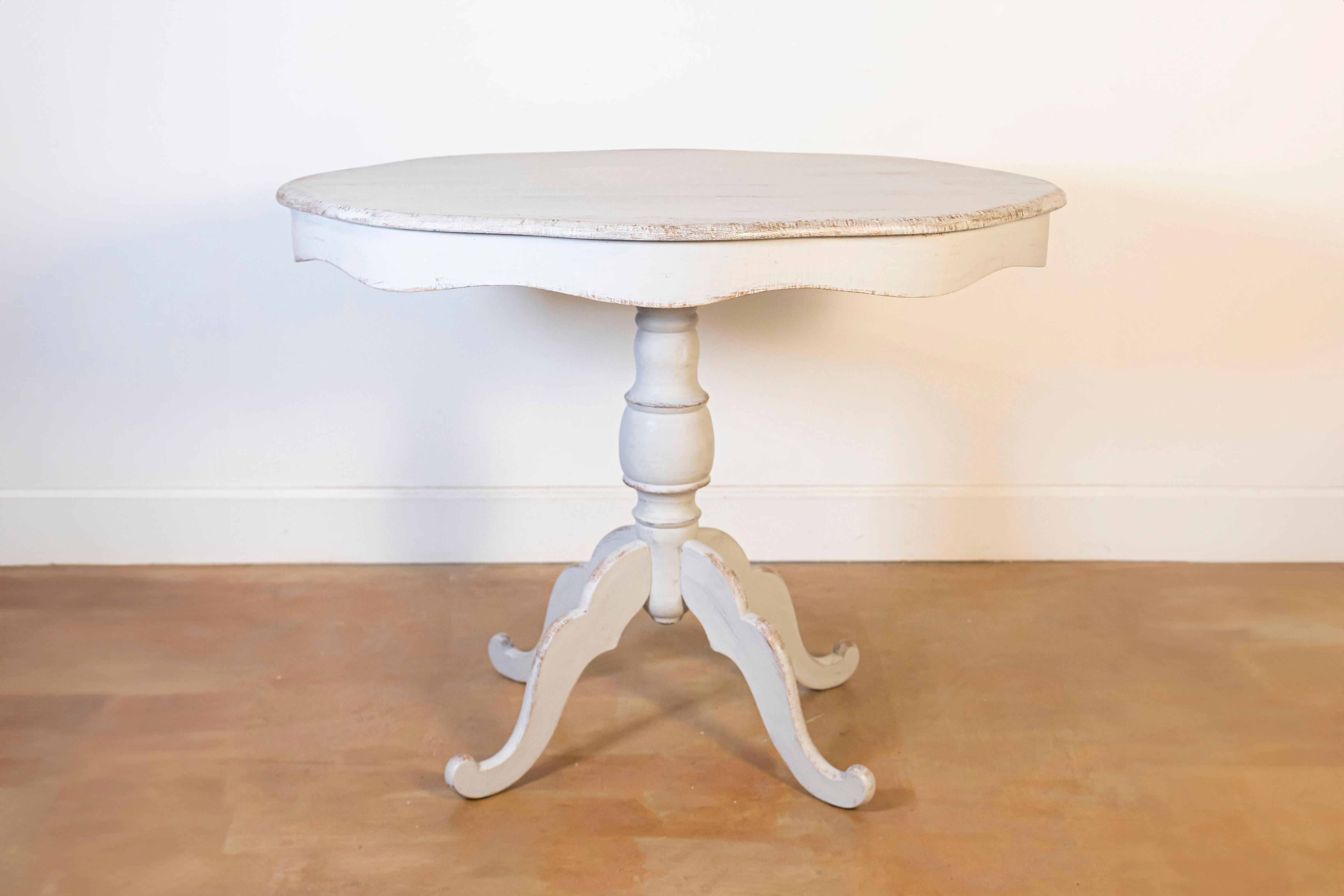A Swedish painted wood oval top pedestal table circa 1860 with carved undulating apron, turned pedestal and quadripod base. Indulge in the allure of Scandinavian design with this charming Swedish painted wood oval top pedestal table, circa 1860. A