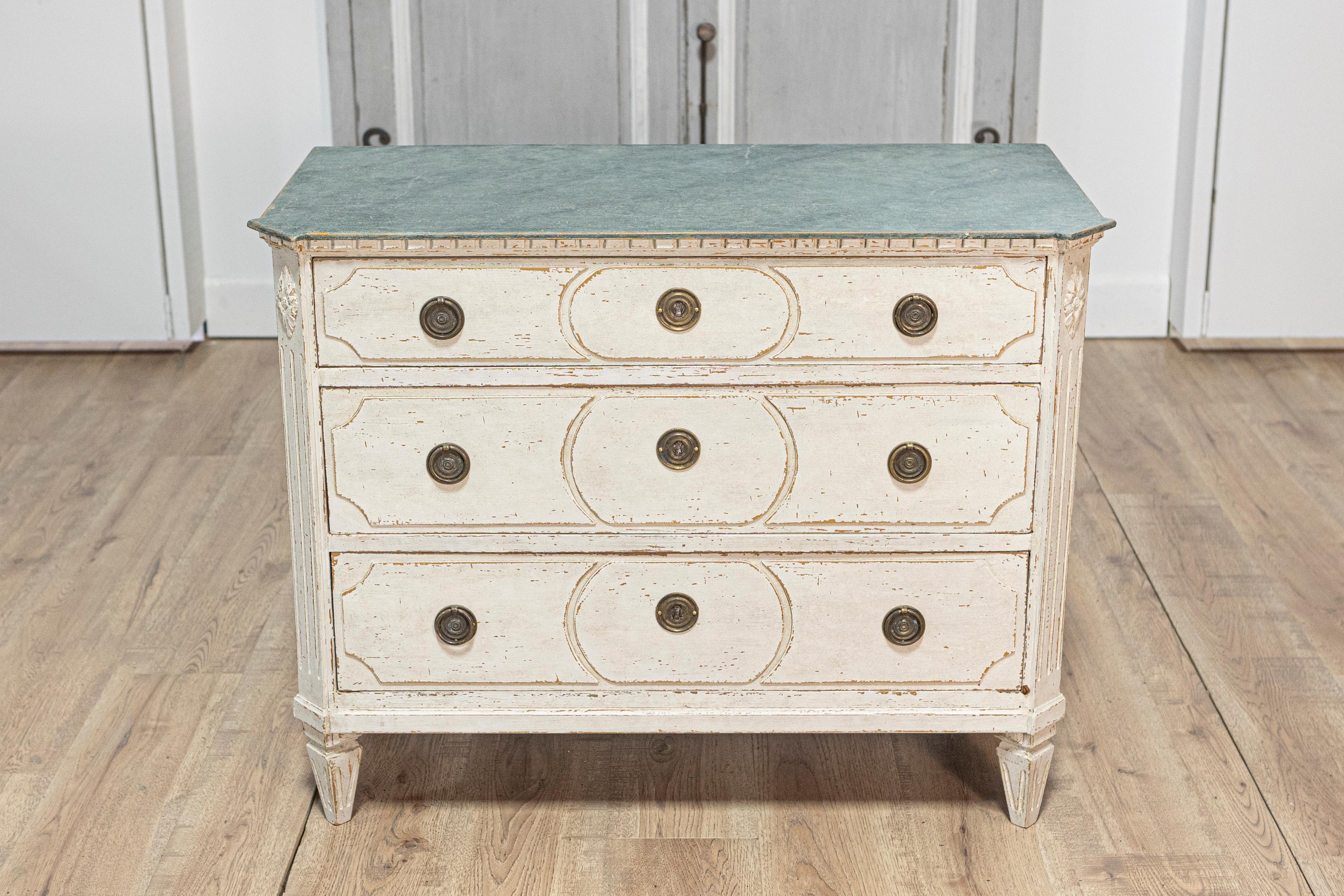 A Swedish Gustavian style painted wood commode from circa 1880 with marbleized top and three drawers. This Swedish Gustavian style painted wood commode from circa 1880 exudes a refined elegance, characterized by its off-white painted finish with