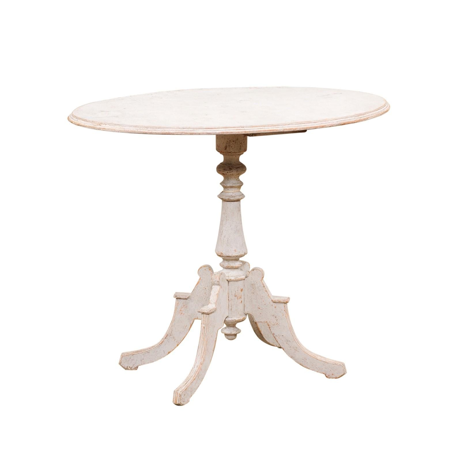 A Swedish painted wood guéridon side table from the late 19th century, with oval top, turned pedestal, quadripartite scrolling base, low finial and distressed patina. Created in Sweden during the last quarter of the 19th century, this painted