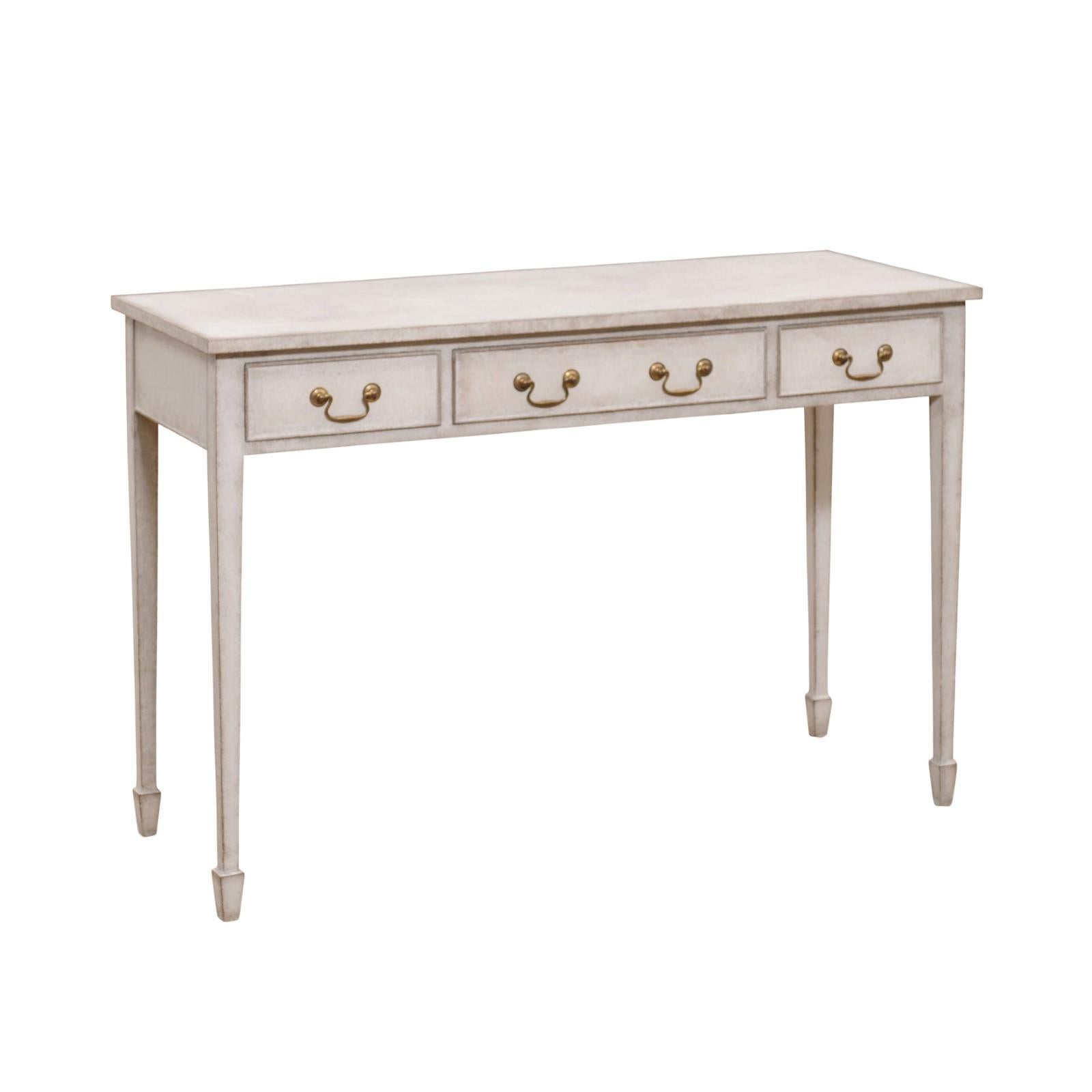 A Swedish painted wood console table from the late 19th century, with three drawers, brass hardware, tapered legs and spade feet. Created in Sweden during the last decade of the 19th century, this elegant painted console table features a simple