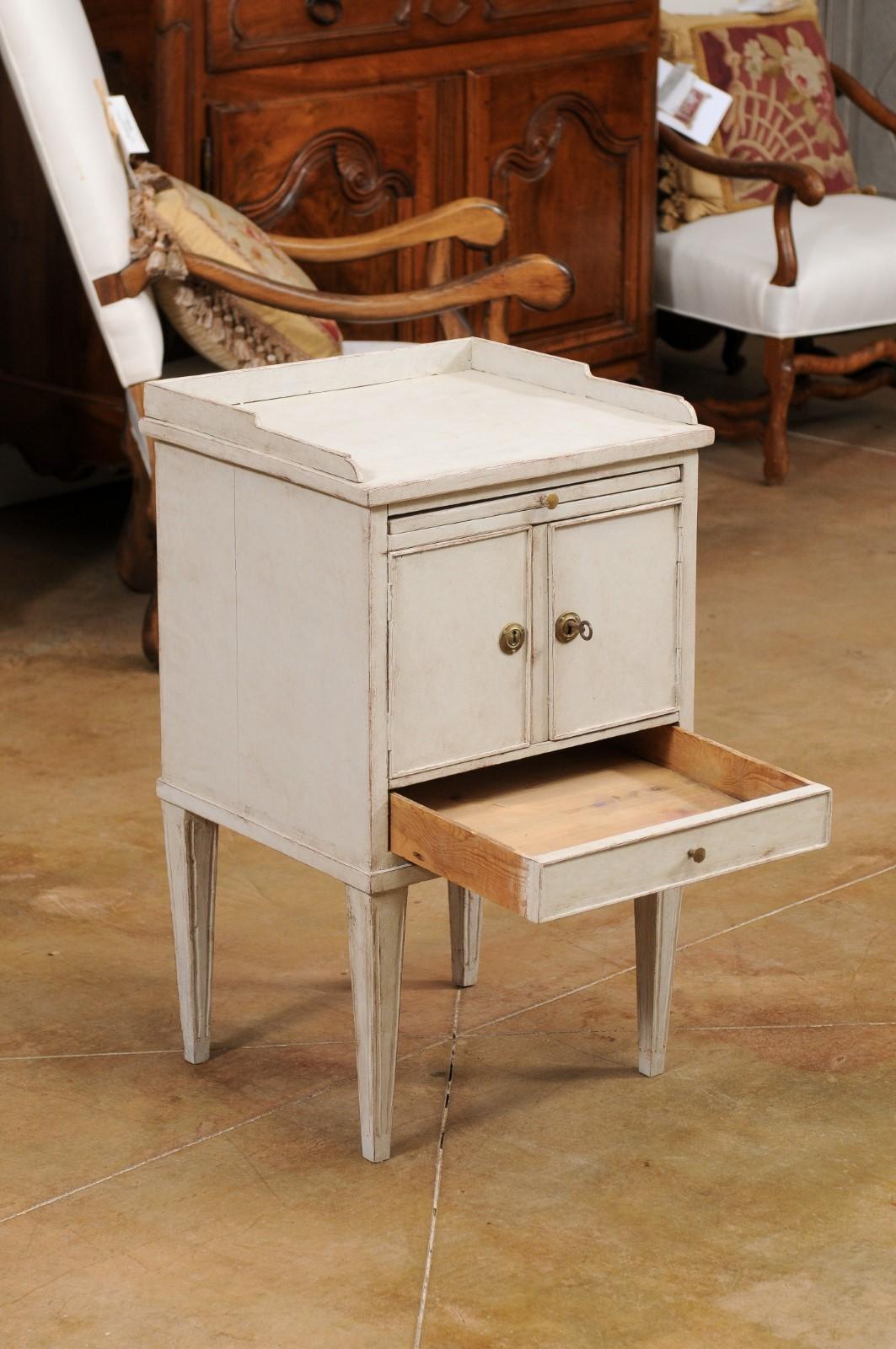 A Swedish painted wood nightstand table from the late 19th century, with doors and drawers. Created in Sweden during the last quarter of the 19th century, this painted bedside table features a rectangular top surrounded by a three-quarter gallery,