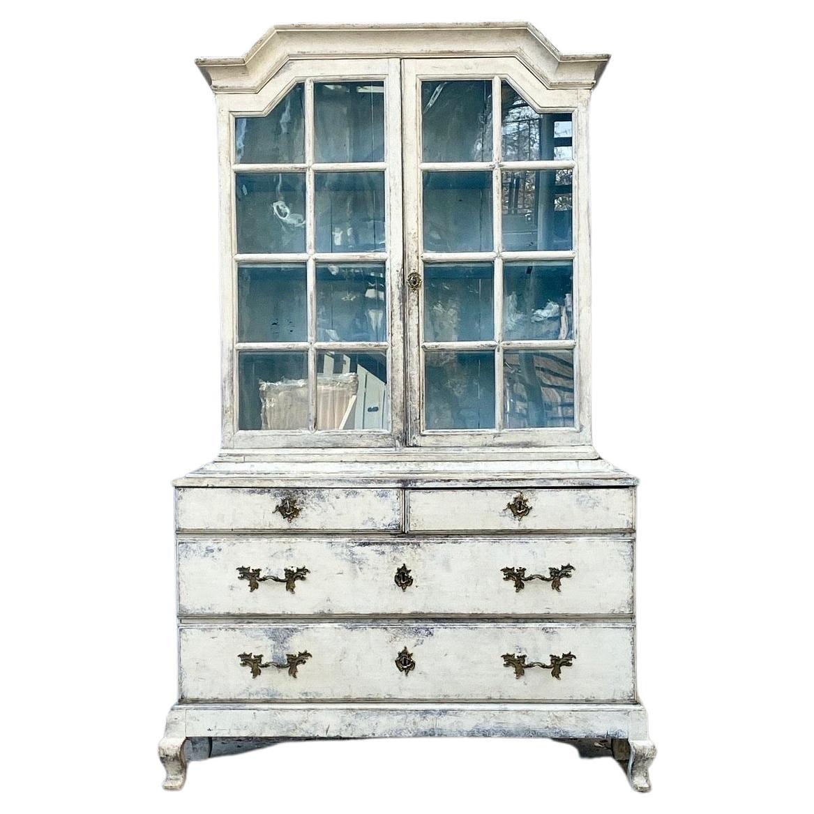 Antique Swedish Glass-Top Cabinet Made in Two-parts.
The base has a set of 4 drawers and the top display cabinet has two glass doors that is patinated in a traditional Gustavian grey and completed with bronze hardware (including a key). The doors to