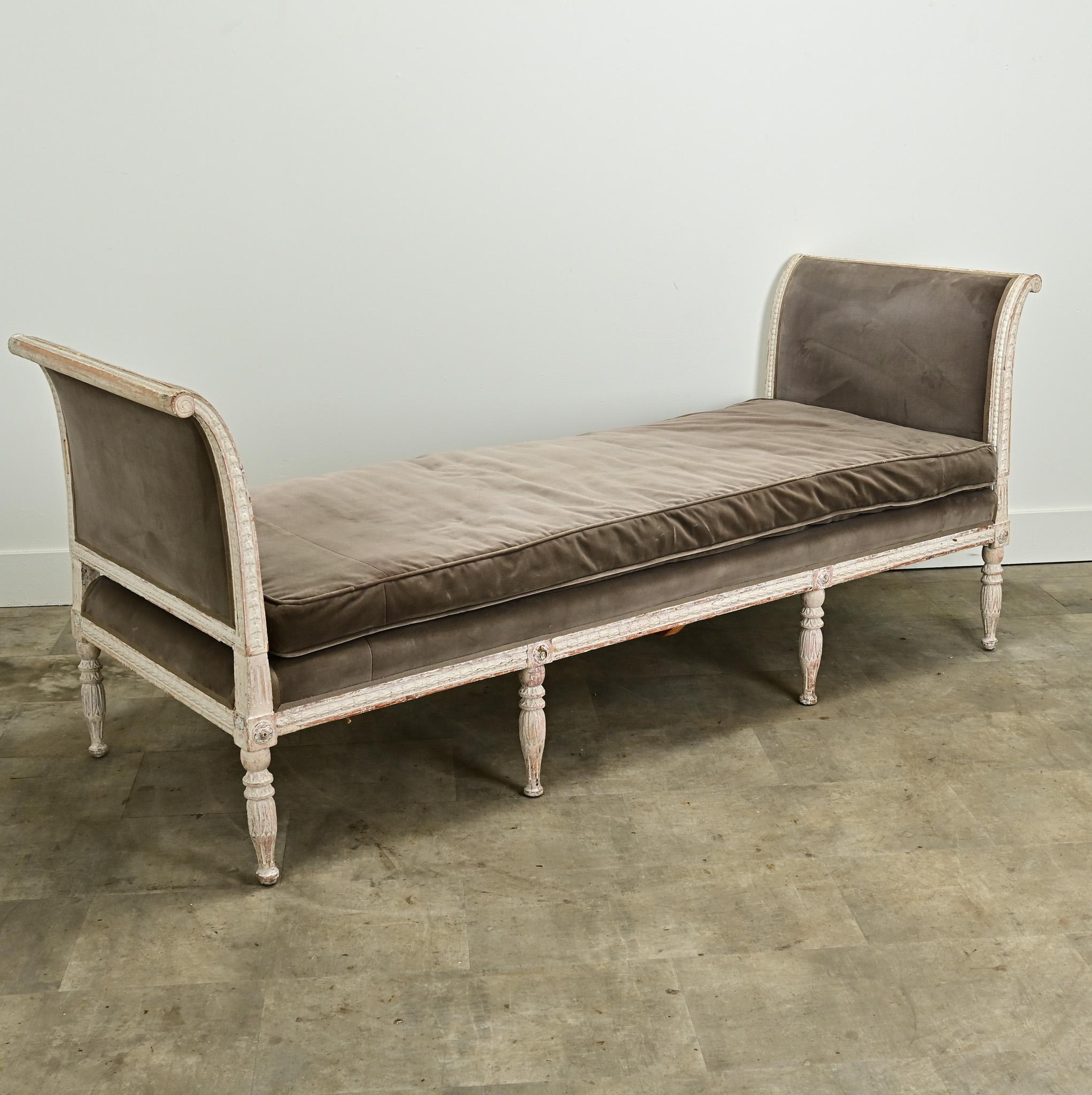 An impressive, long Swedish 18th Century Louis XVI daybed. The sides of this daybed are the same height and are carved with Louis XVI style motifs. The bed frame is upholstered in a comfortable worn velvet, matching its removable cushion. This