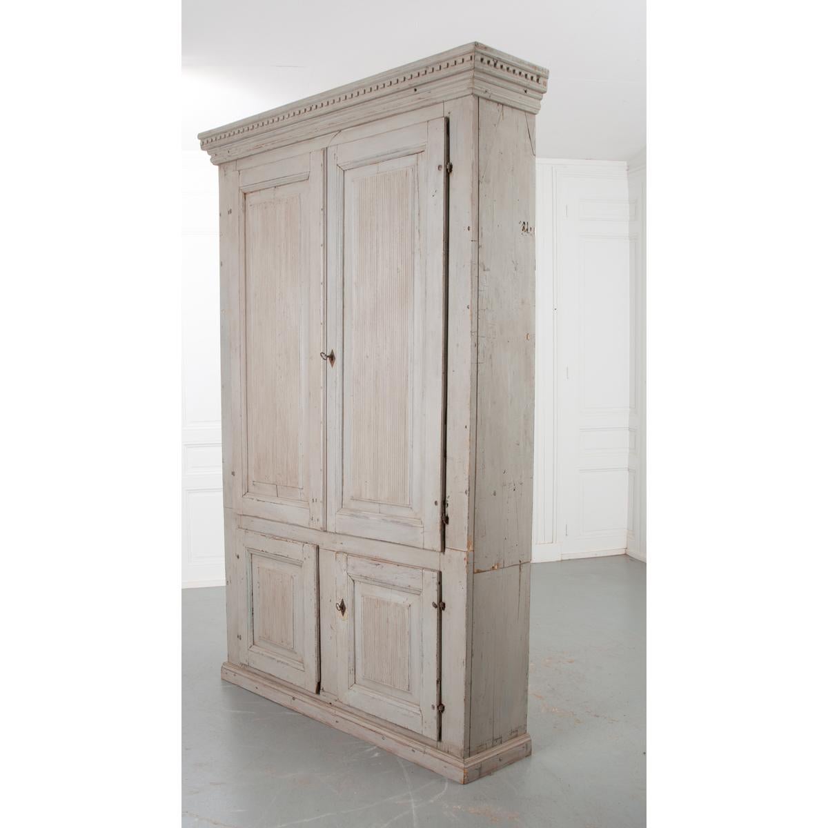 This is a massive cabinet from 18th century Sweden, circa 1780. A wonderful patina covers the whole, still sporting its original light blue paint. Deeply carved squares protrude from the cornice perimeter. All four door panels feature ribbed carving