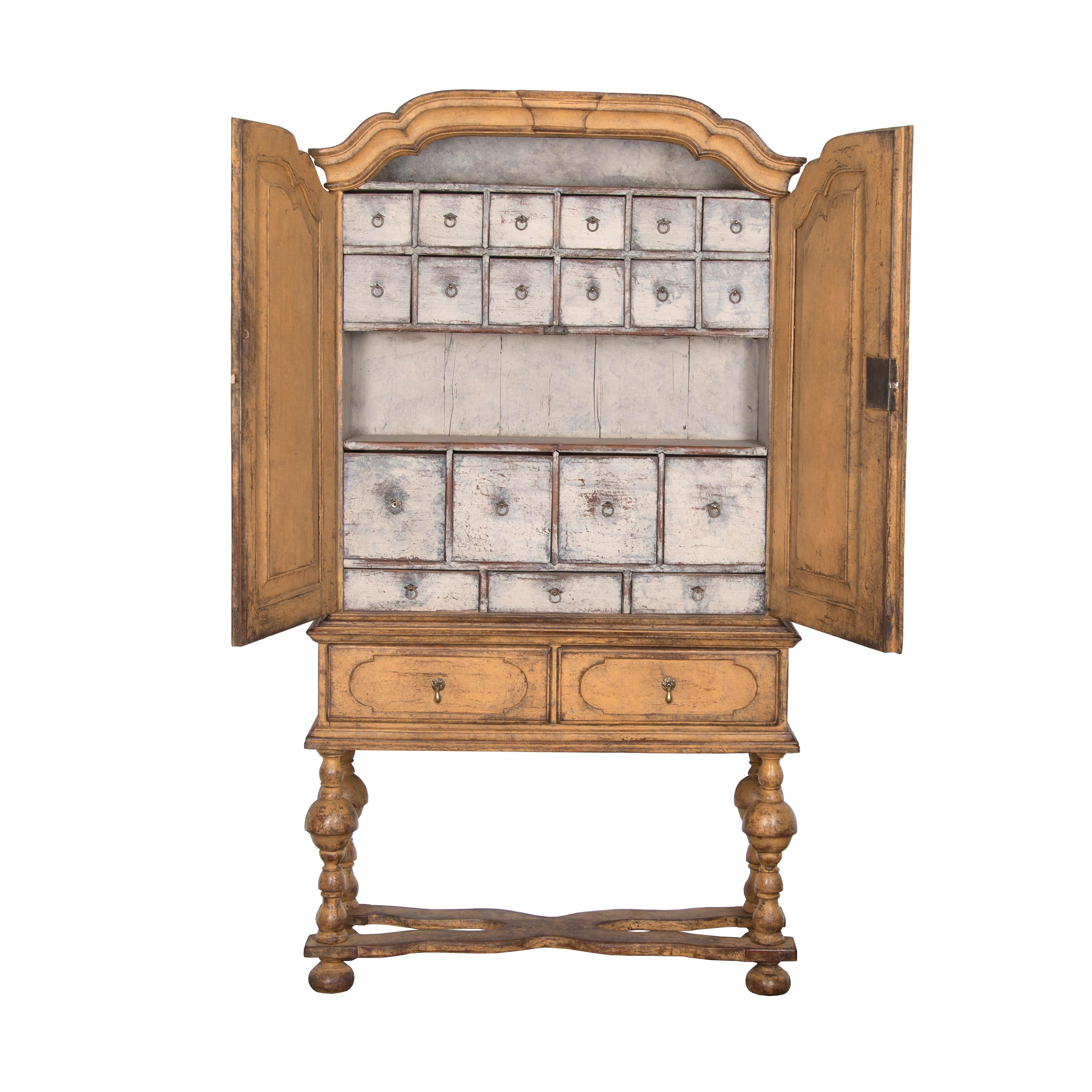Swedish 18th century two part cabinet with a decorative carved pediment. Two doors with carved detailing to the front and sides open to various spice drawers, and below are two drawers with further carving. This piece features carved turned legs and