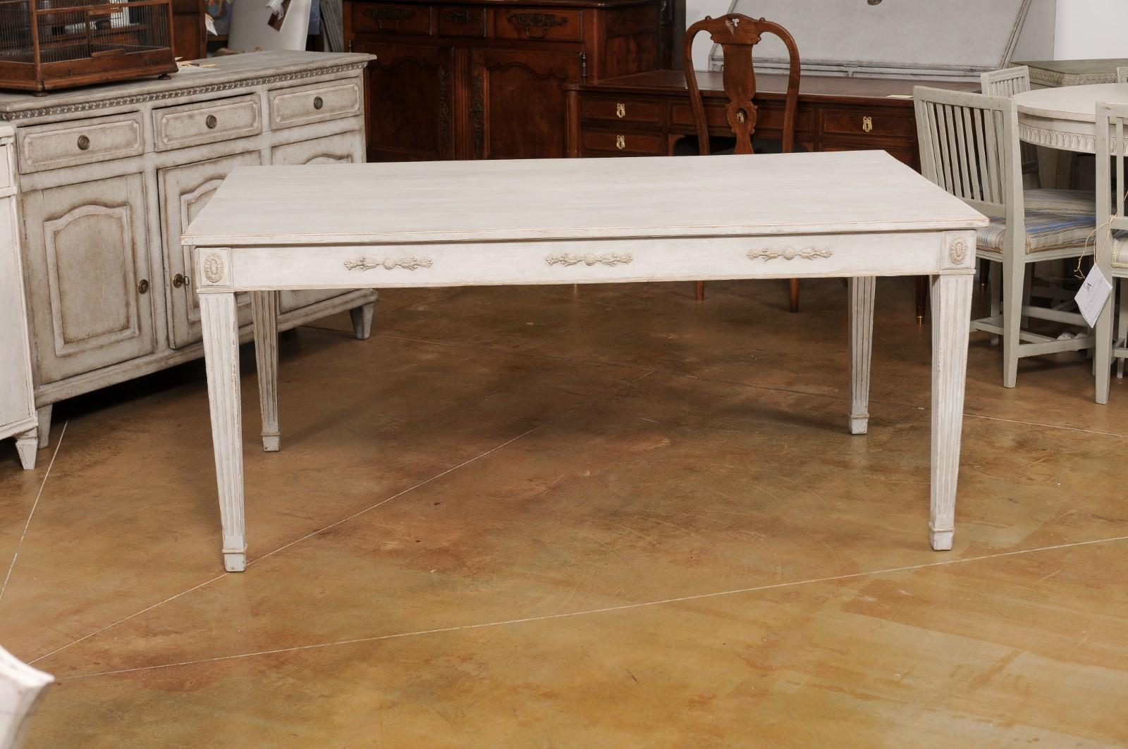 A Swedish Gustavian style painted wood dining table from the early 20th century with carved apron (measuring 25.25