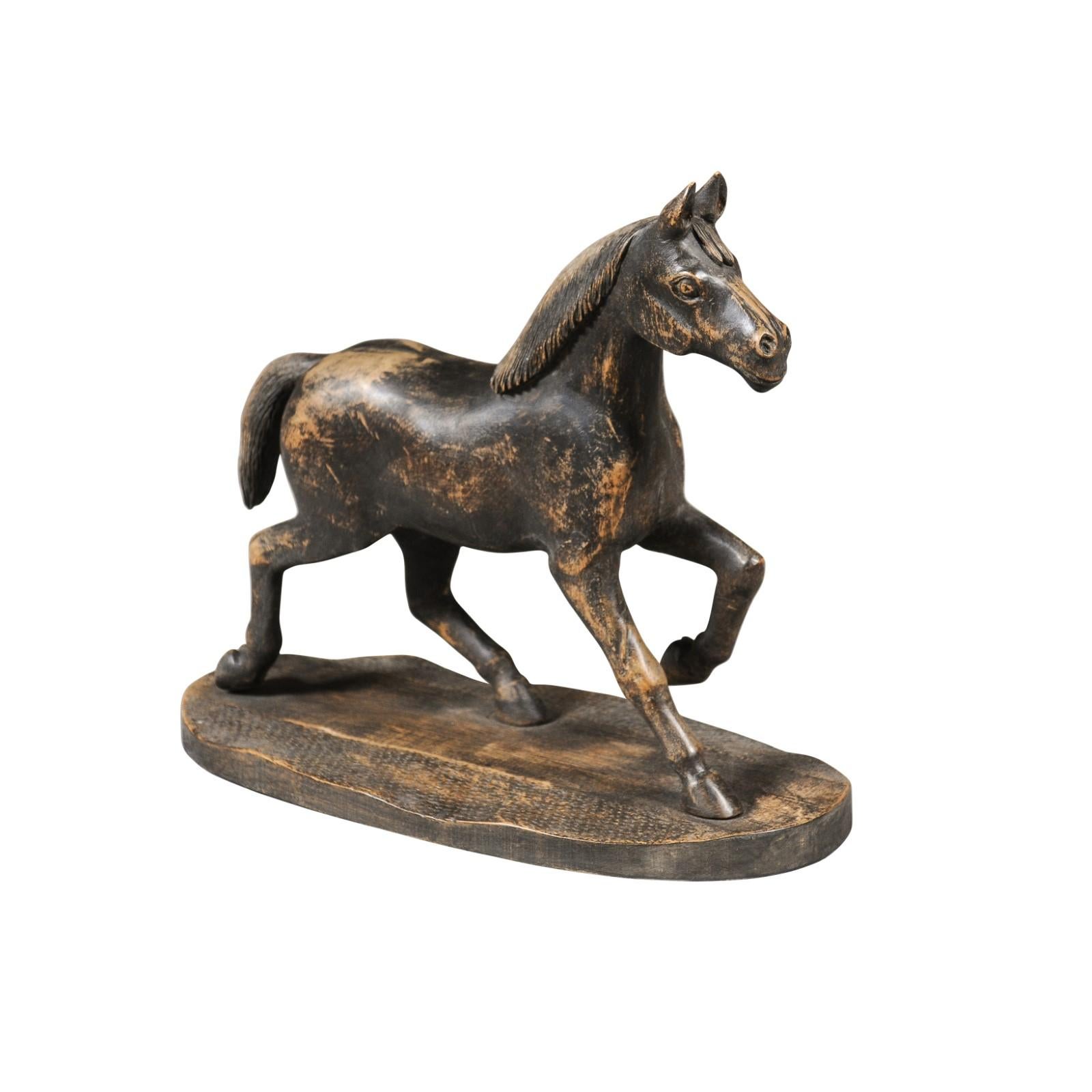 A small Swedish carved wooden horse sculpture on base from the early 20th century with dark distressed patina. Created in Sweden during the early years of the 20th century, this petite sculpture charms us with its elegant subject and weathered