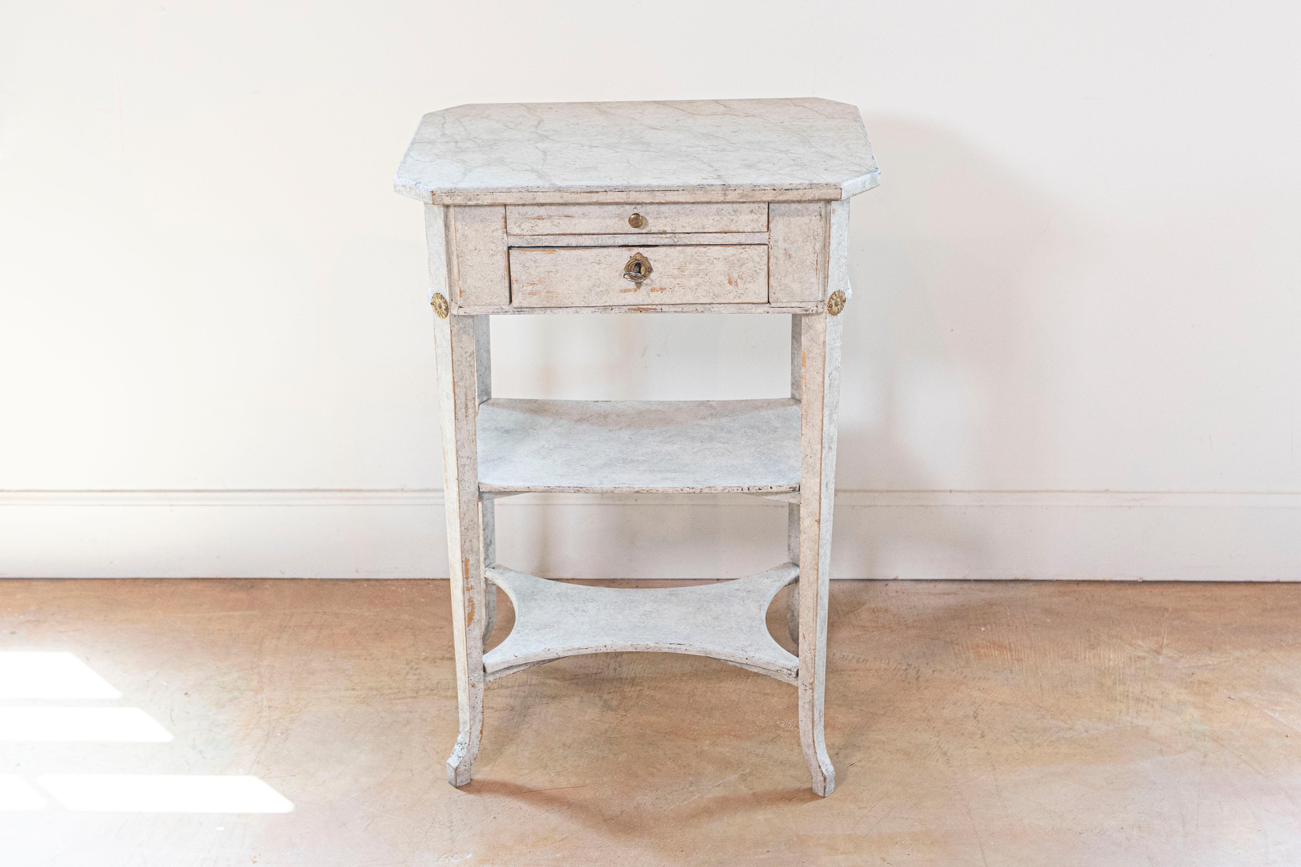 A Swedish Gustavian style painted wood console table from the early 20th century with faux marble top, two drawers, brass rosettes, two shelves and curving feet. Created in Sweden during Turn of the Century which saw the transition between the 19th