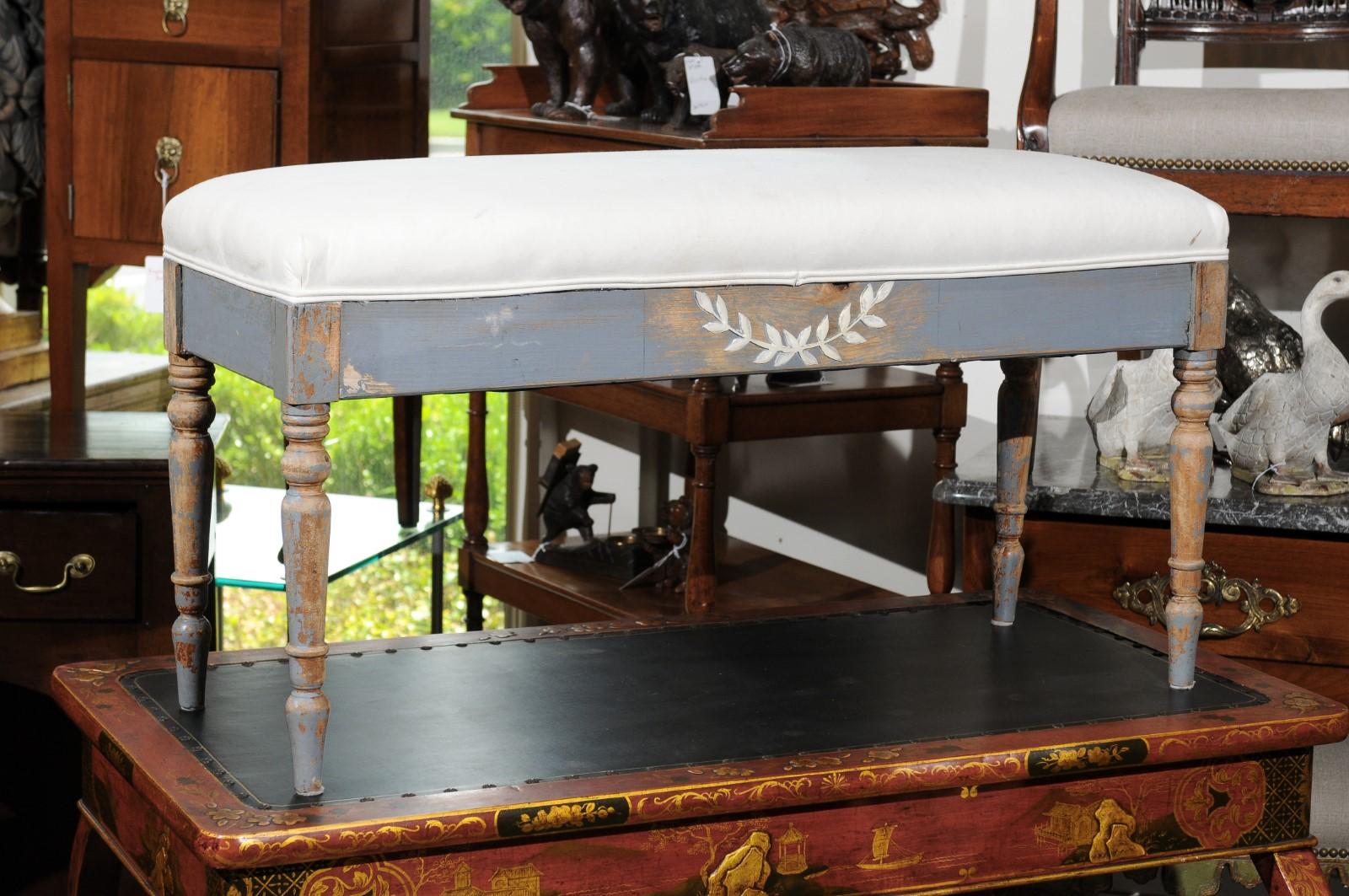 A Swedish neoclassical style painted wood bench from the early 20th century, with laurel wreath accent, cylindrical legs and new upholstery. Born in Sweden during the first quarter of the 20th century, this exquisite neoclassical style painted bench