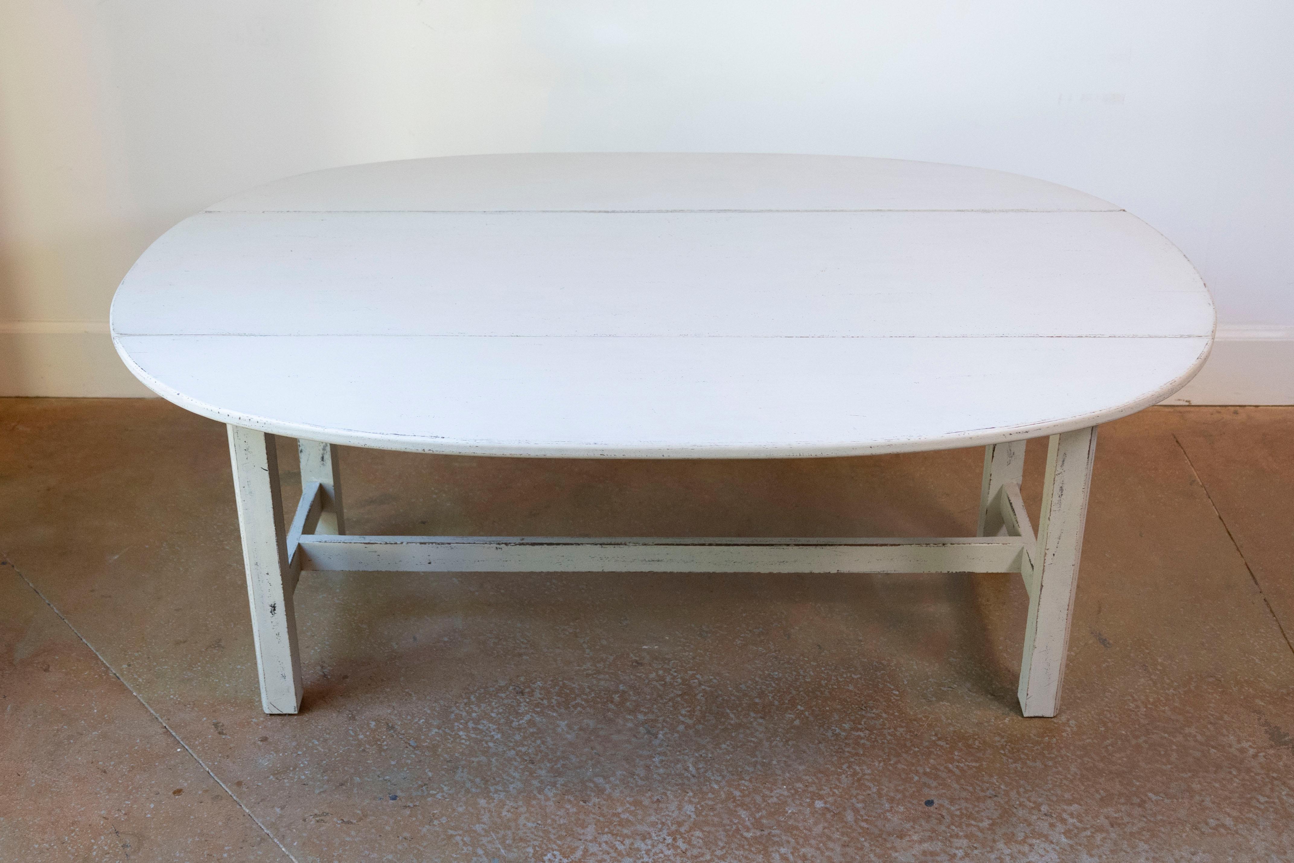 A Swedish drop-leaf coffee table from circa 1920 with creamy gray painted finish, oval top and H-Form stretcher. Embrace the versatility and timeless elegance of this Swedish drop-leaf coffee table from circa 1920, a piece that masterfully combines