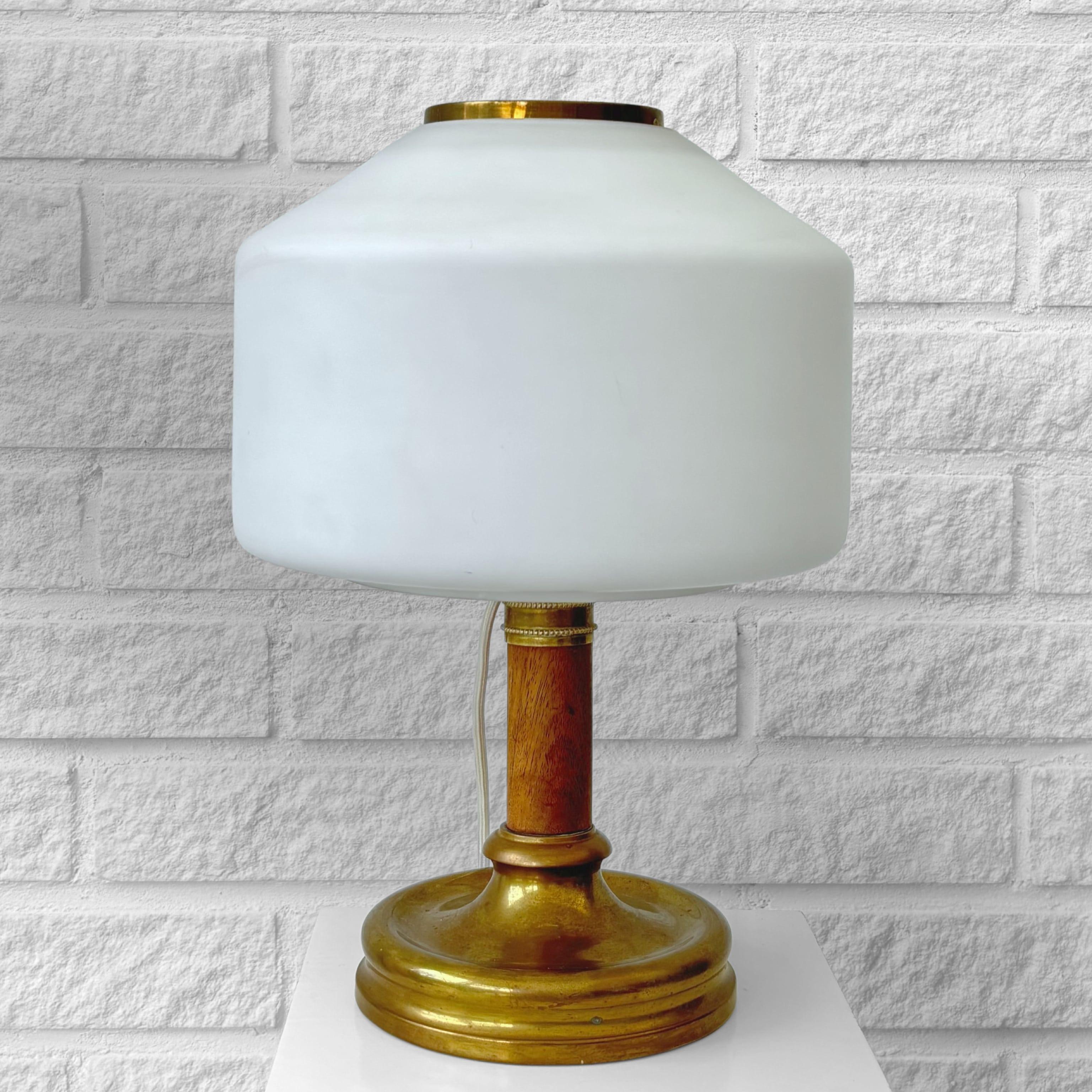 Lampada da tavolo degli anni '20 prodotta da Arvid Böhlmarks Lampfabrik, caratterizzata da un pilastro cilindrico in legno massiccio di Oak incastonato su una base circolare in ottone. Il diffusore in vetro bianco è fissato da un paralume in ottone