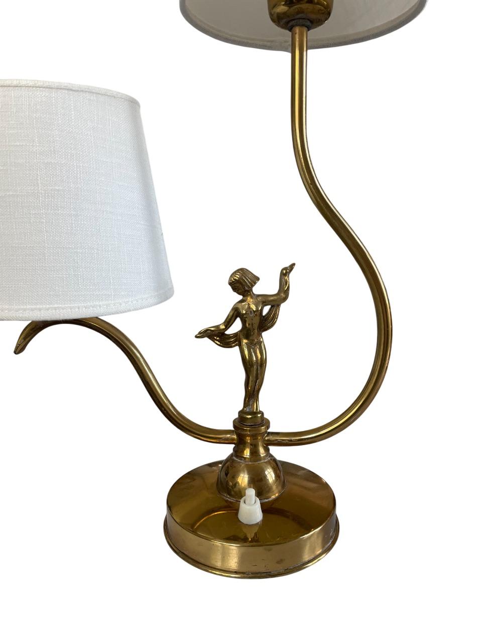 A charming and sculptural brass table lamp by Ystad-Metall, Sweden, dating to the 1930s. This elegant piece features a distinctive double-arm design with two sweeping curves supporting fabric lampshades. At the center stands a beautifully detailed