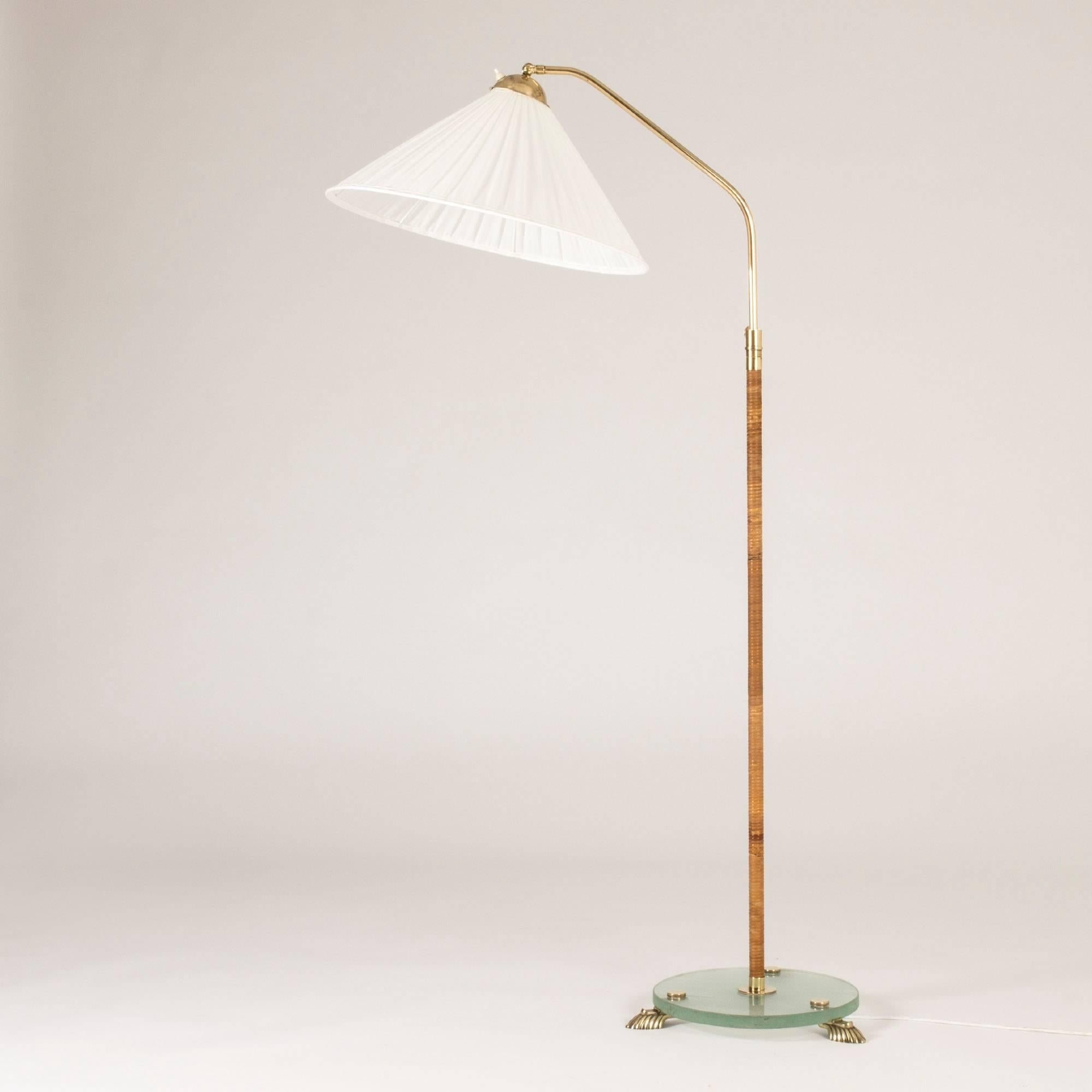 Beautiful floor lamp, made in Sweden in the 1930s. Made with a frosted glass base and brass lions’ feet and rattan wound brass handle. Lovely, refined design and details.