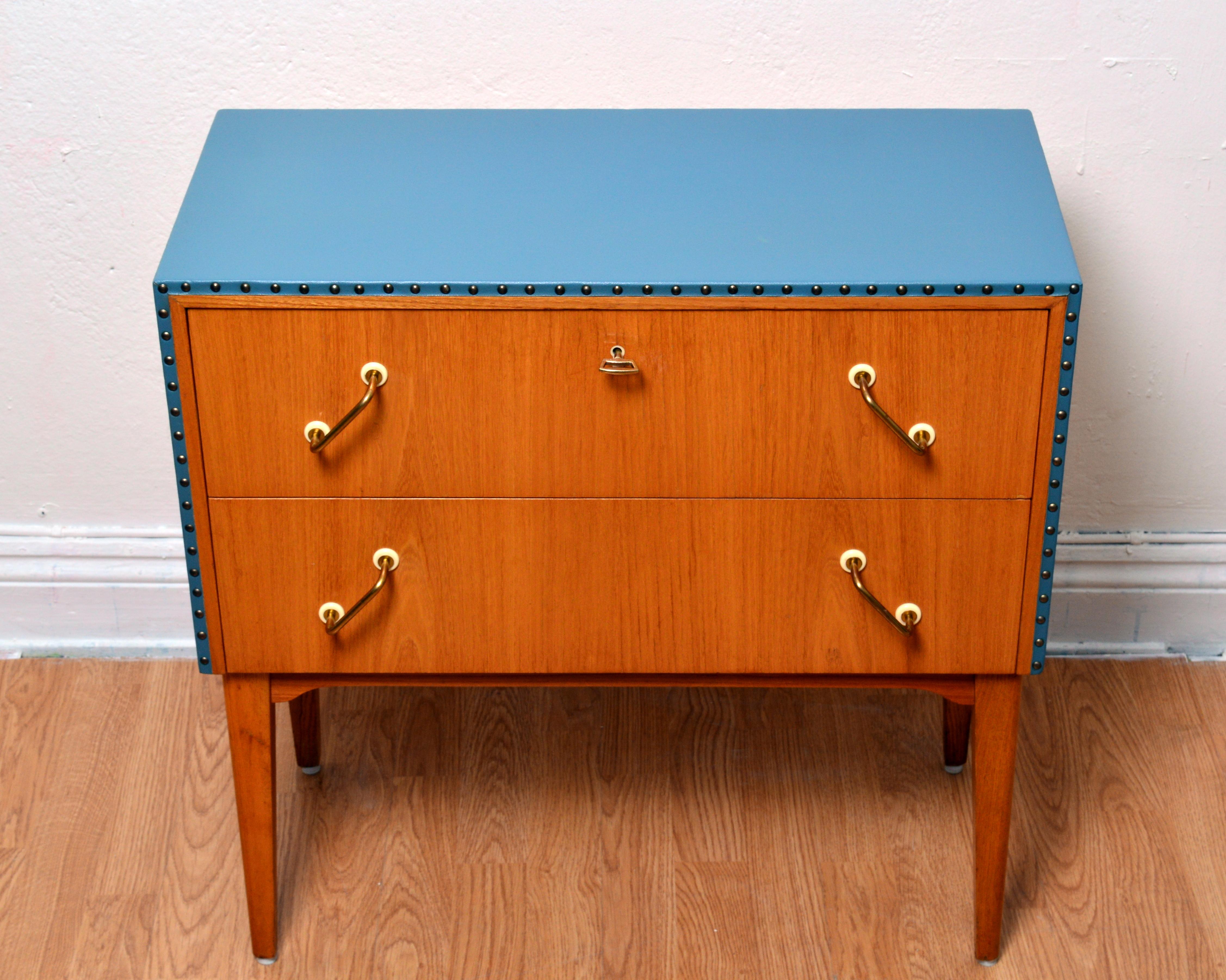 Petite swedish chest of drawers / two drawer cabinet in the style of Swedish designer Otto Schulz. Top nnd sides upholstered with light blue faux leather / leatherette with brass studs edging. Original handles and key in solid brass. Excellent
