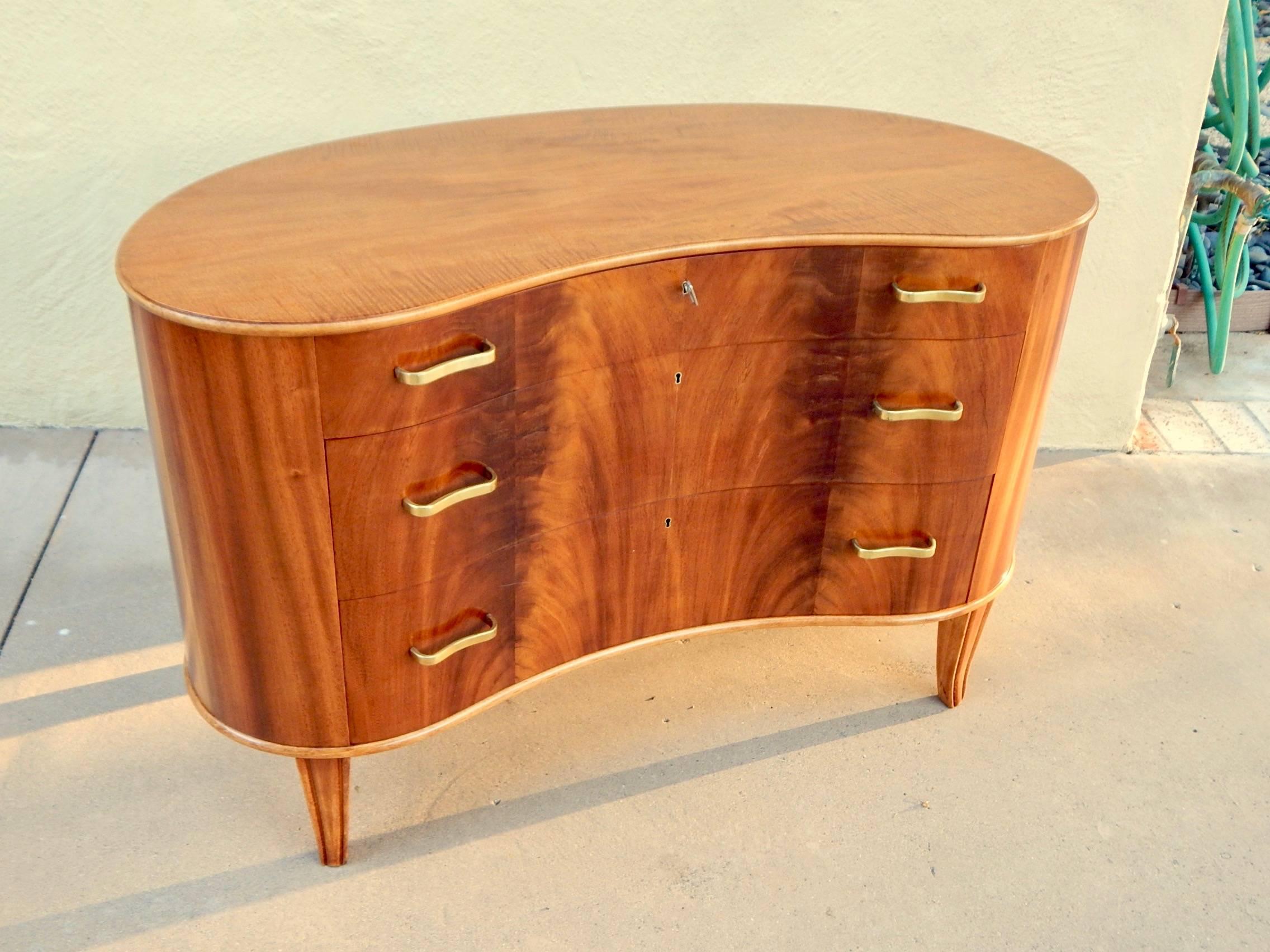Swedish 1940s moderne kidney shaped chest of drawers rendered in highly figured, book matched Santo Domingo mahogany. With four saber legs. All original metal pulls. 
This chest has just been beautifully restored by our craftsmen. Tagged, Ferdinand