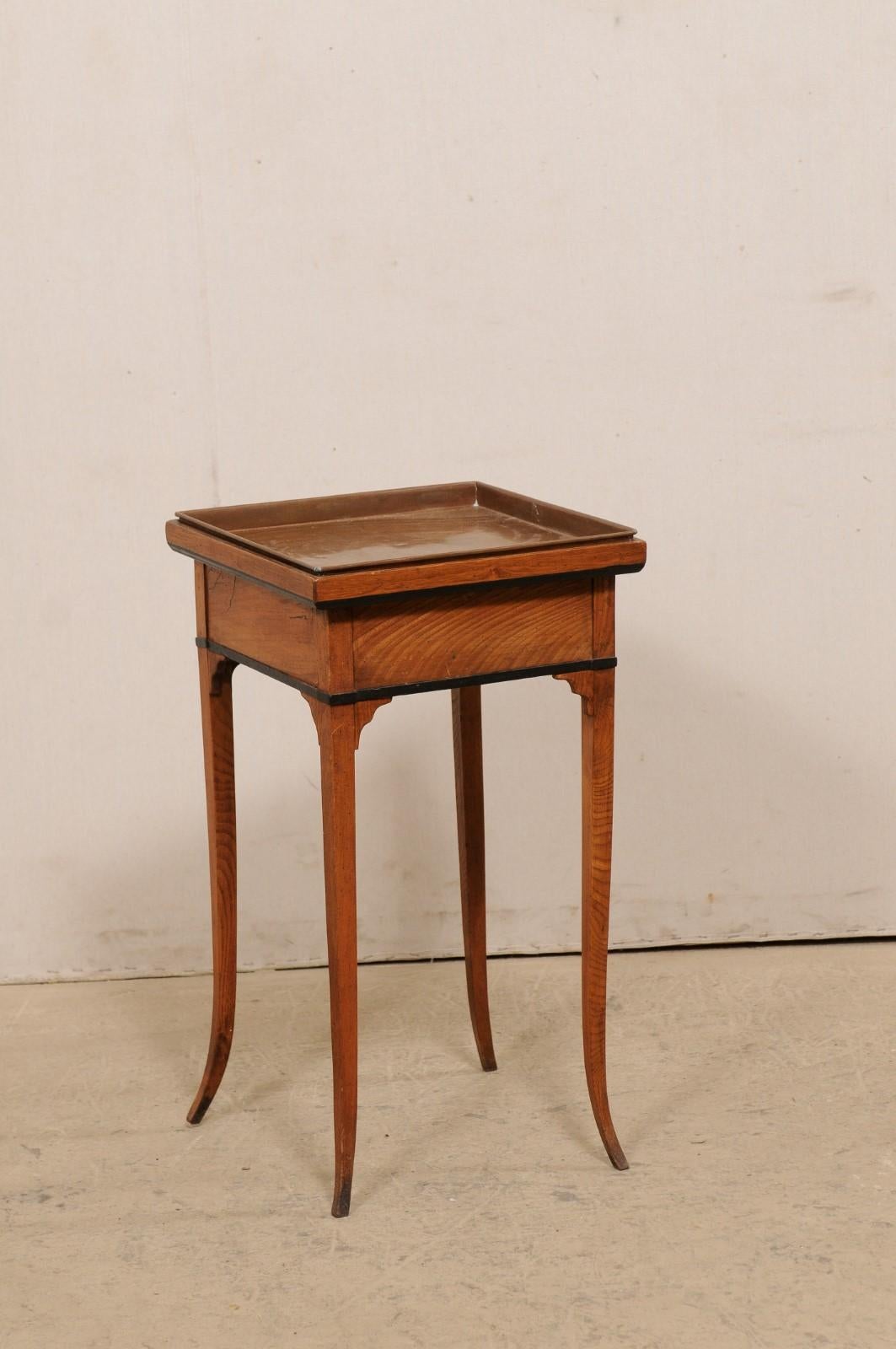 A Swedish wooden side table with removable copper tray top from the 19th century. This antique table from Sweden features a square-shaped top, which has a copper metal tray recessed within the top, which when removed, offers storage beneath. The