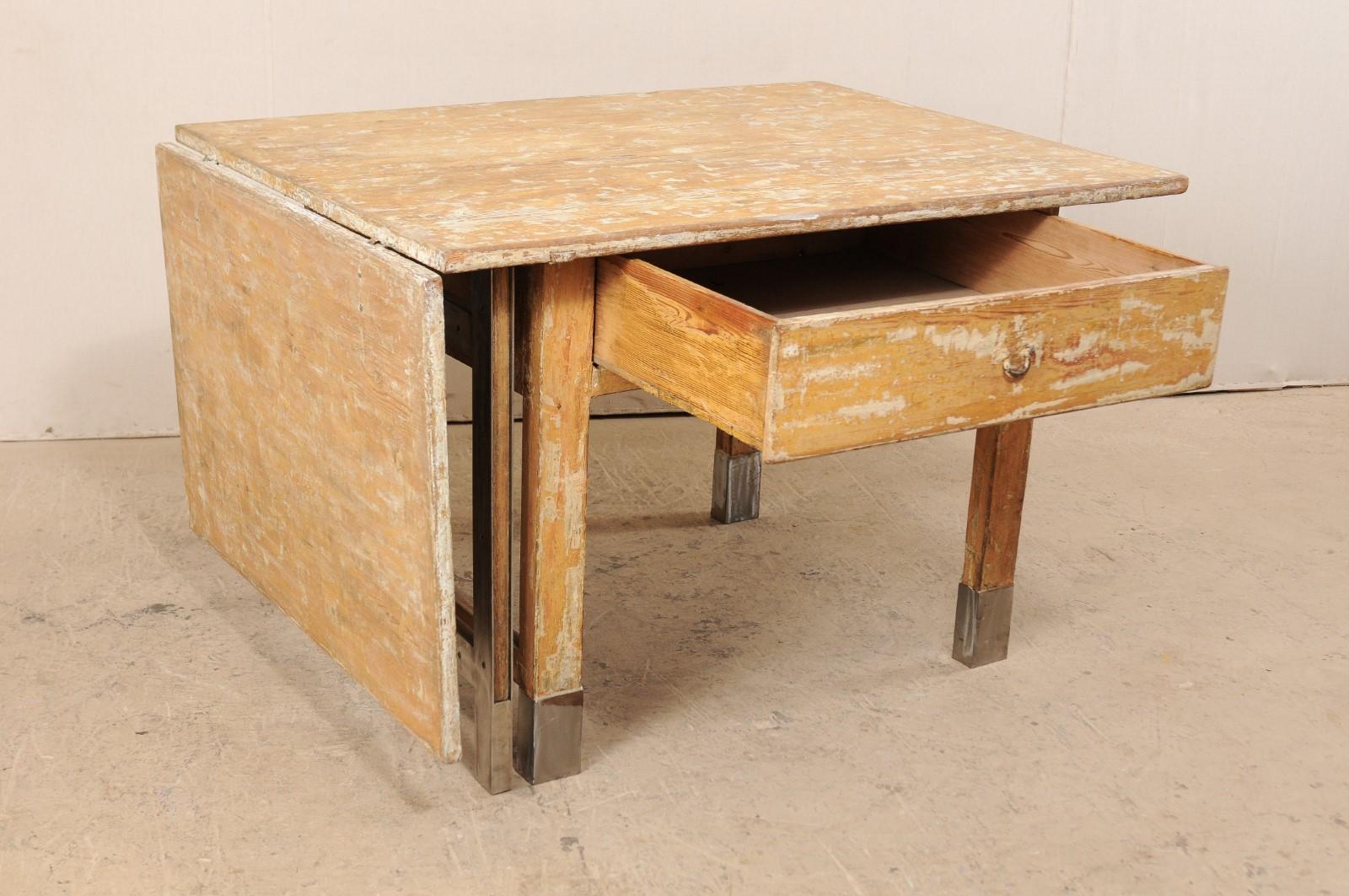 A Swedish gate leg table from the 19th century with contemporary additions. This antique farmhouse style table from Sweden features a rectangular-shaped top with single drop leaf and gate leg extension at one side, and a single drawer set into the