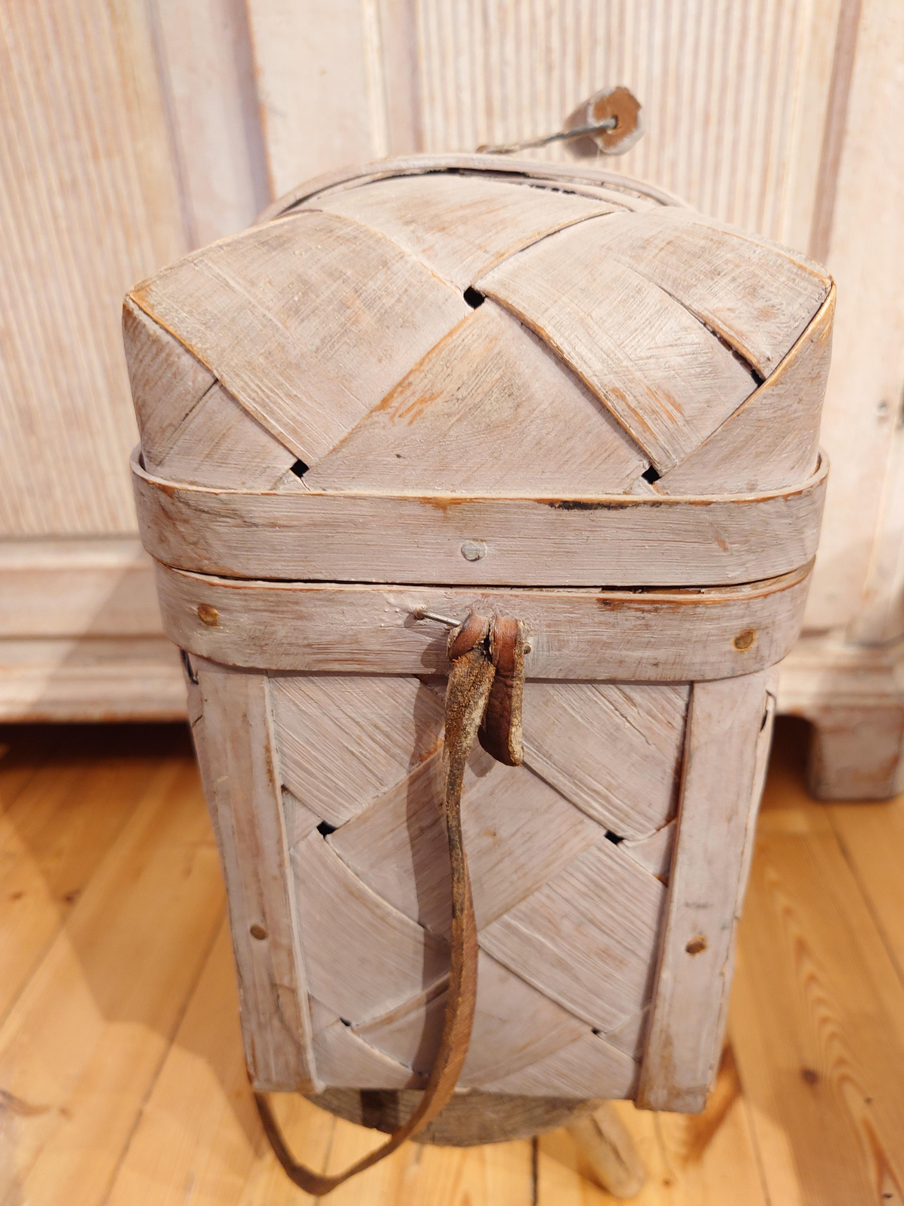 Swedish 19th century woven pine basket circa 1890.

Beautiful rustic made pine basket using strips of pine fixed into a pine frame. Complete with original lid.
Beautiful original paint.

Fitted with a handle on the top.
There is a leather strap so