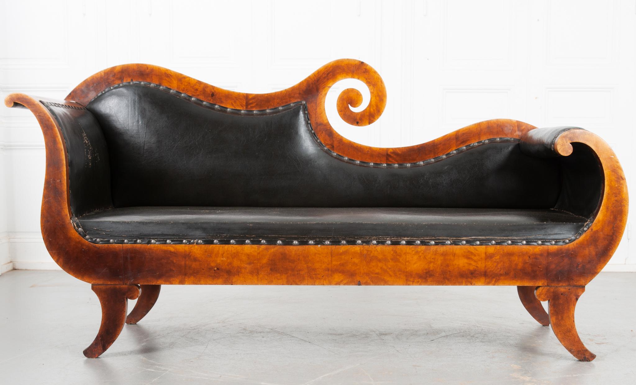 This curvilinear settee is from Sweden circa 1830 and made of striking birchwood. The worn leather has a patina and has been made soft and supple over the last few centuries. Decorative honeycomb nailheads secure the leather upholstery in place. The