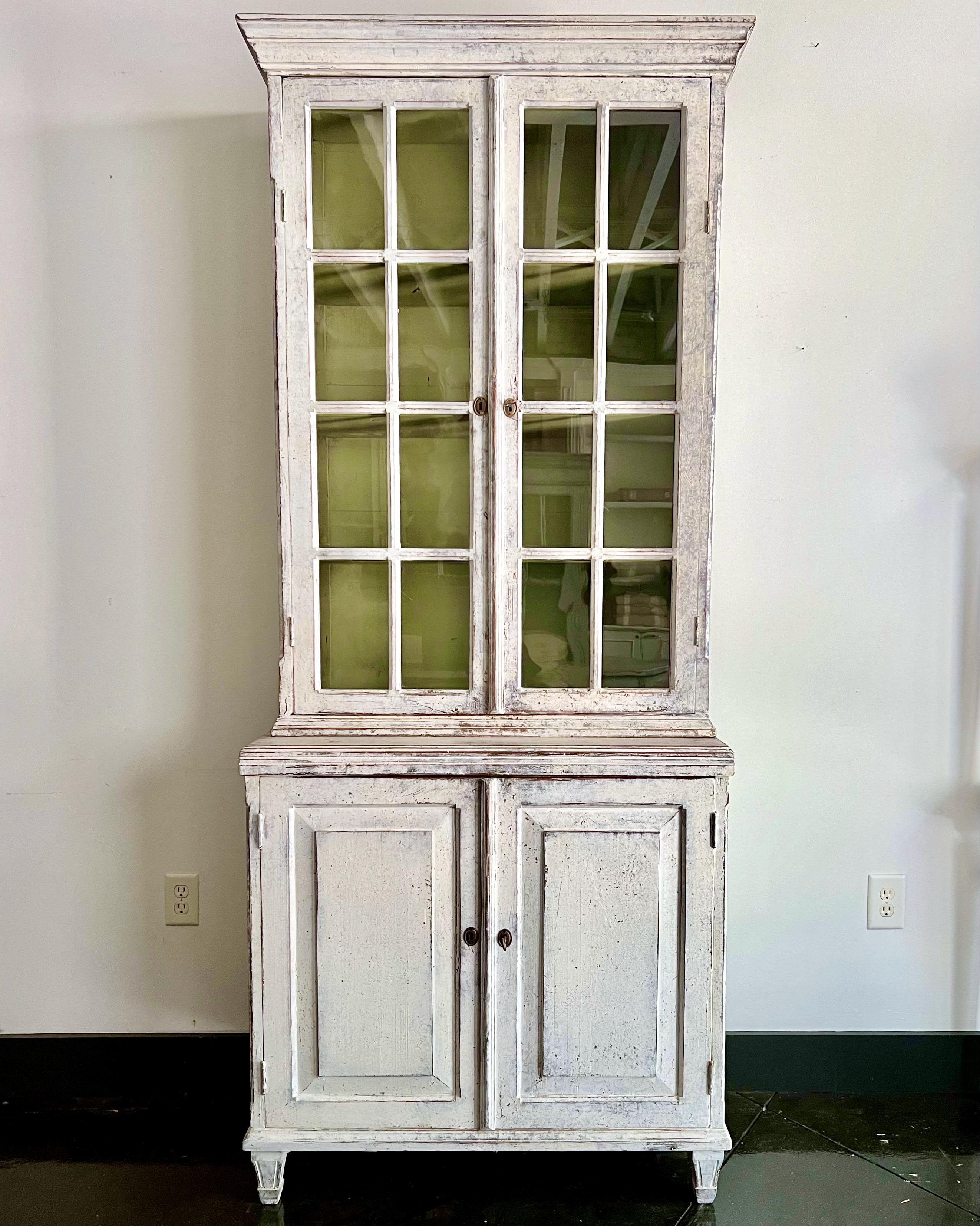 19th century Swedish cabinet with glass fronted doors in late Gustavian style.
Upper library section with molded cornice, four moveable shelves behind double glass doors.
The lower cabinet with molded door fronts and one shelf. All resting on carved