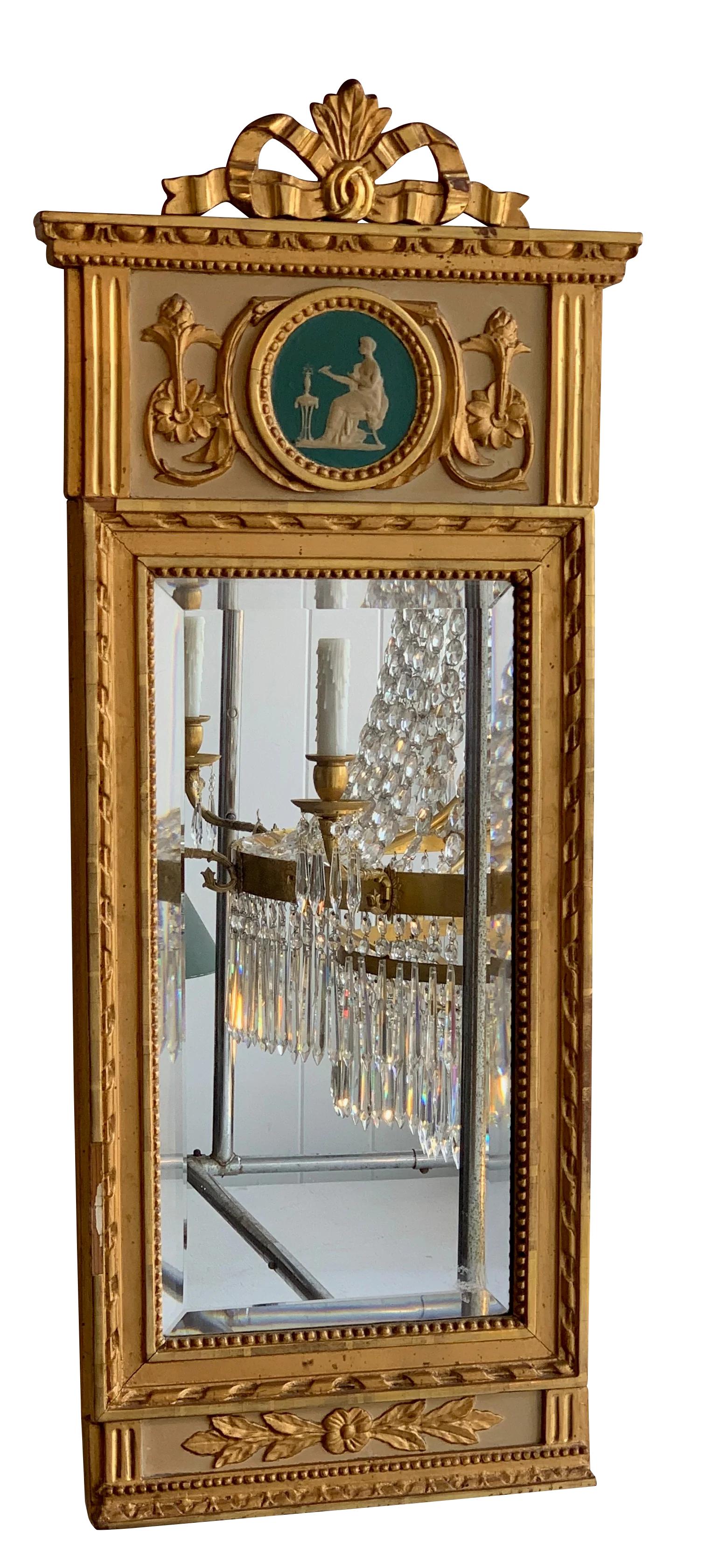 Swedish 19th Century Gilded mirror, having a ribbon crest above the crown molding over a classical jasperware medallion over a beveled mirror over a foliate panel. 

