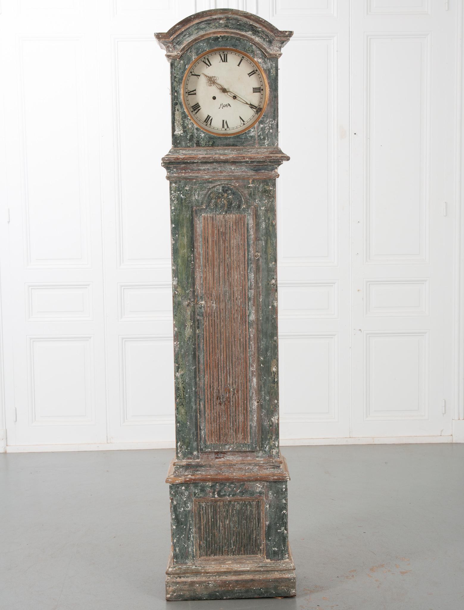 A fantastic example of a Swedish 19th century long case Mora clock! Layers of white and dark greenish blue paint cover the whole, giving it a fantastic patina. A bonnet shaped crown tops the clock, nicely complimenting the circular clock face.