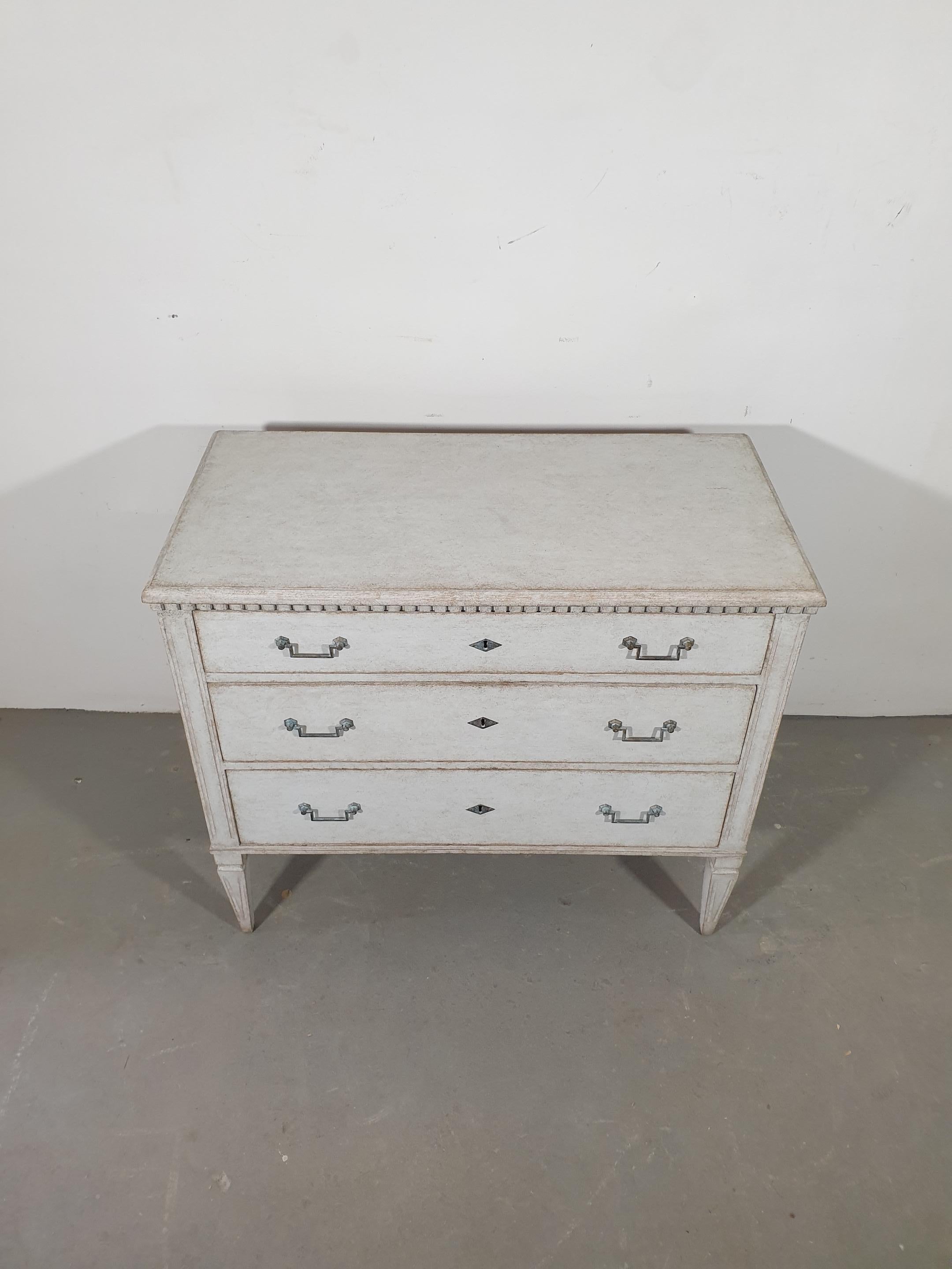 A Swedish Gustavian style three-drawer chest from the 19th century with carved dentil molding and tapered legs. This Swedish Gustavian style three-drawer chest from the 19th century is an elegant piece that beautifully captures the essence of the