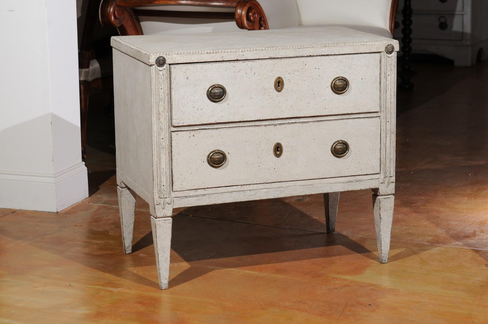 A Swedish Gustavian style painted wood two-drawer chest from the 19th century, with carved motifs and rosettes. Created in Sweden during the 19th century, this painted chest features a rectangular top with beaded motifs, sitting above two drawers