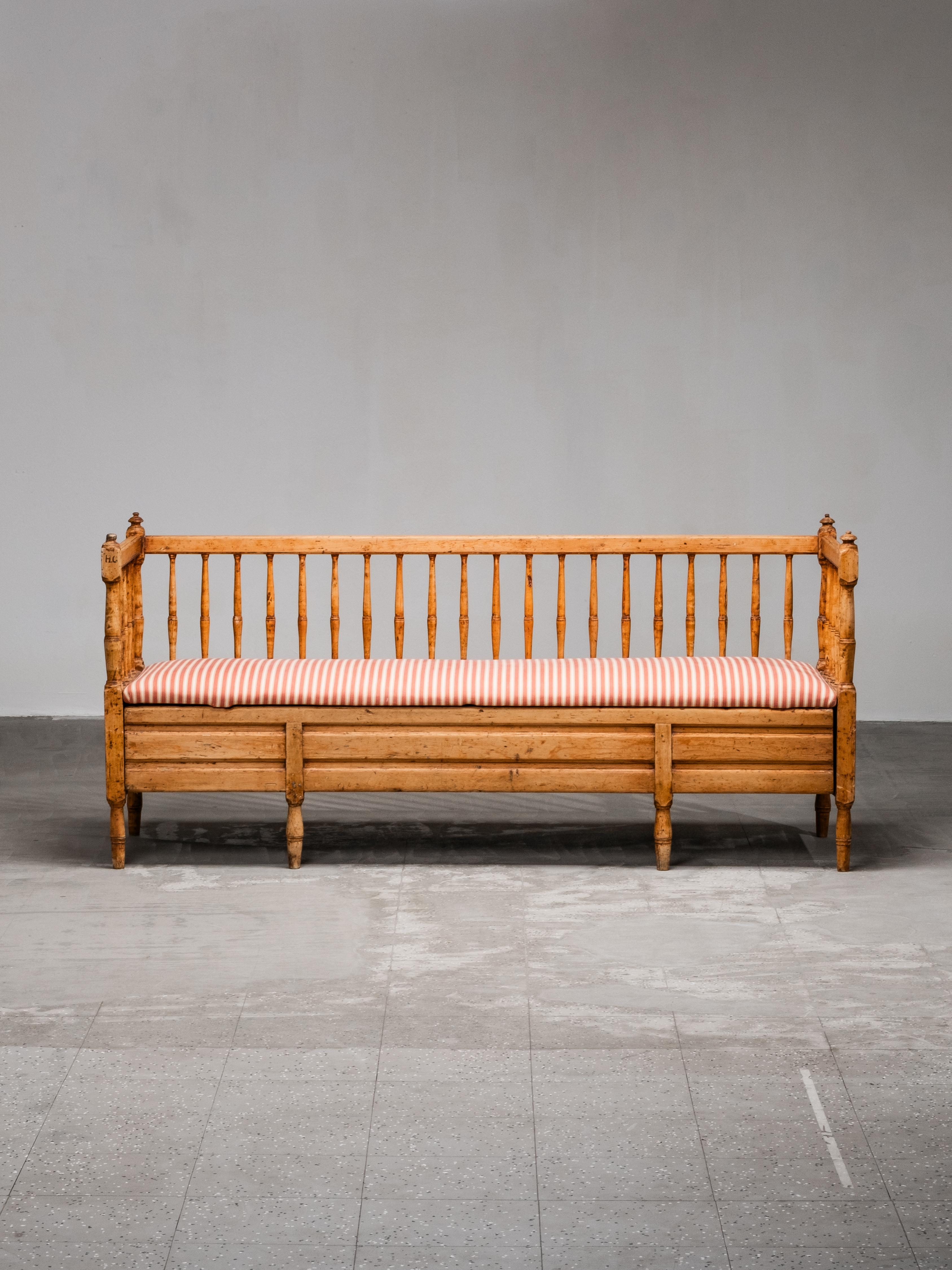 Sofá-banco sueco gustaviano del siglo XIX, bellamente envejecido, que muestra el carácter artesanal y el encanto rústico típicos del mobiliario rural de la época. El armazón es de pino macizo con respaldos y patas de husillo torneado, todo ello con