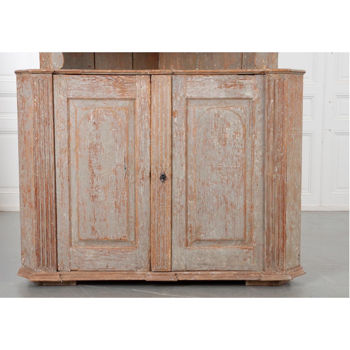 This handsome corner cabinet from 19th century Sweden is constructed with a characteristic neoclassical shape. The worn light blue paint is original to the piece and gives it a wonderful patina. A nicely carved cornice tops the whole, with