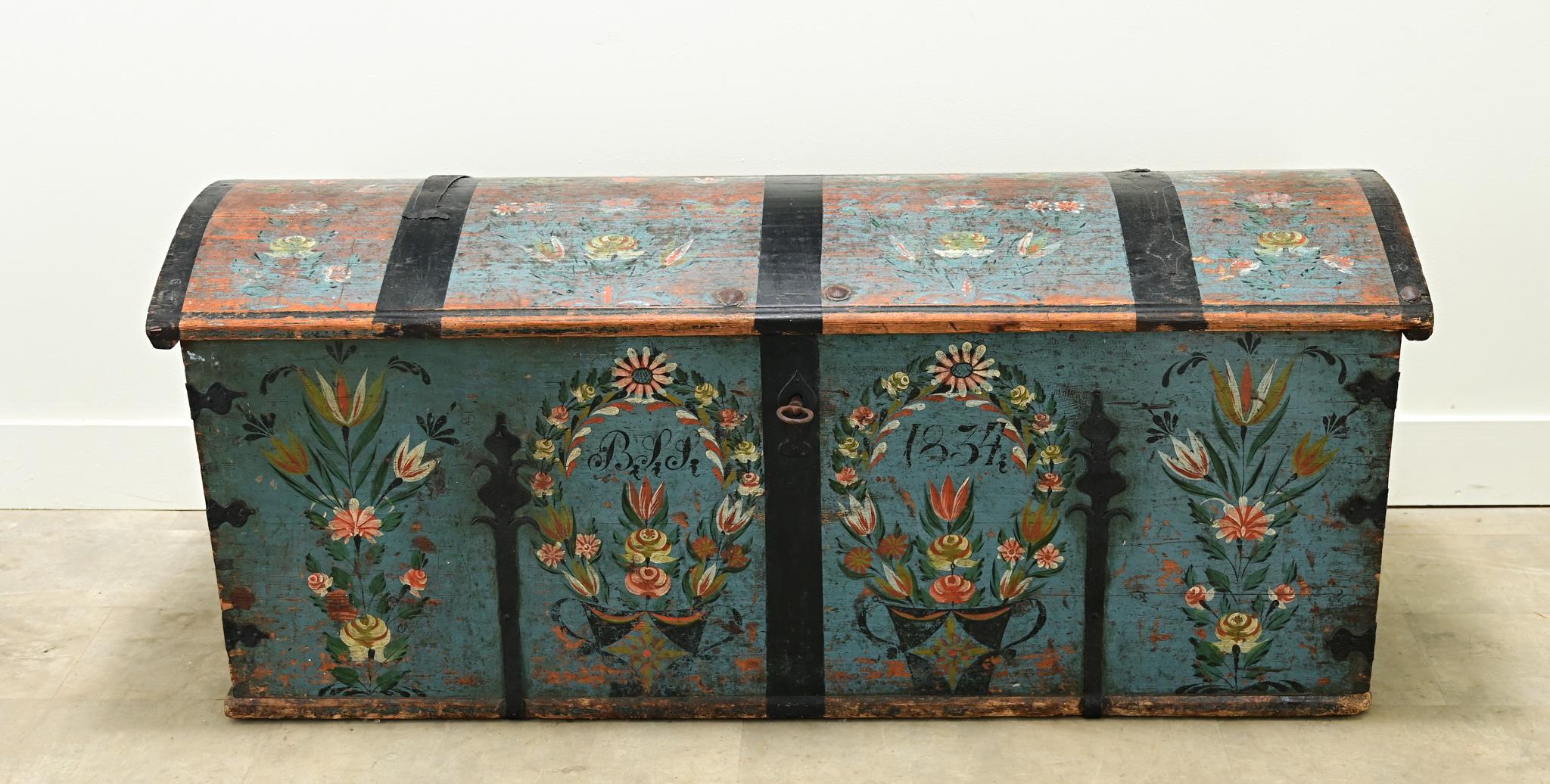 A large 19th century iron bound painted marriage trunk. The exterior of this truck is painted blue with colorful flower baskets and arrangements on its facade with the monogram, “B S S” and the date, 1834. The dommed truck top is painted with floral