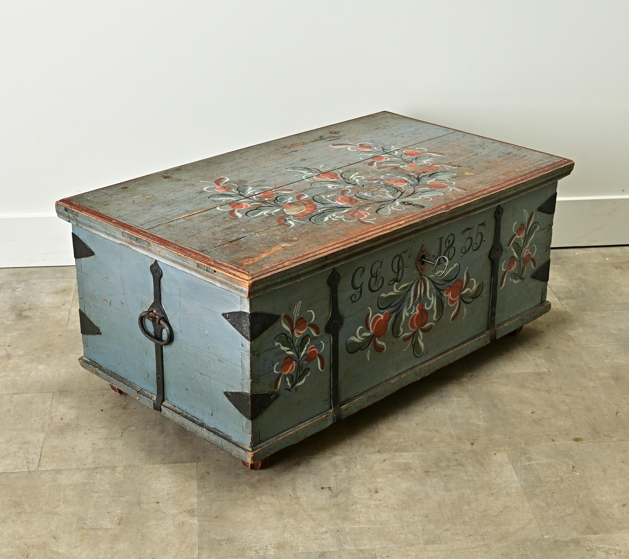 A petite Swedish pine marriage trunk with its original paint. The exterior is painted blue with floral designs and monogrammed G E D 1835. Forged iron bindings enforce the construction of this hardwood trunk with large handles on each end. The top