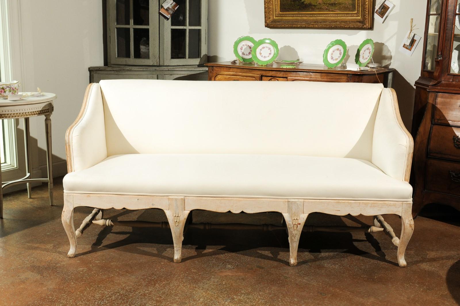A Swedish painted wood sofa from the 19th century with turned cross-stretcher and new upholstery. This charming Swedish sofa features a simple straight back, flanked by two arms accented with a delicate scrolling movement on their upper rails and