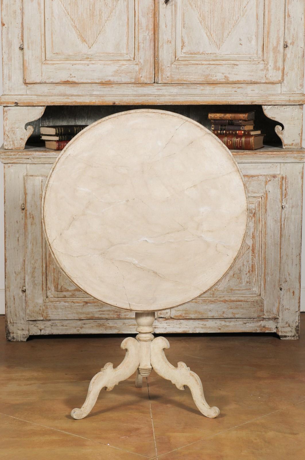 A Swedish Rococo style painted tilt-top table from the 19th century, with carved tripod base. Created in Sweden during the 19th century, this Rococo style table features a circular faux marble tilt-top folding down for convenient storage. The table