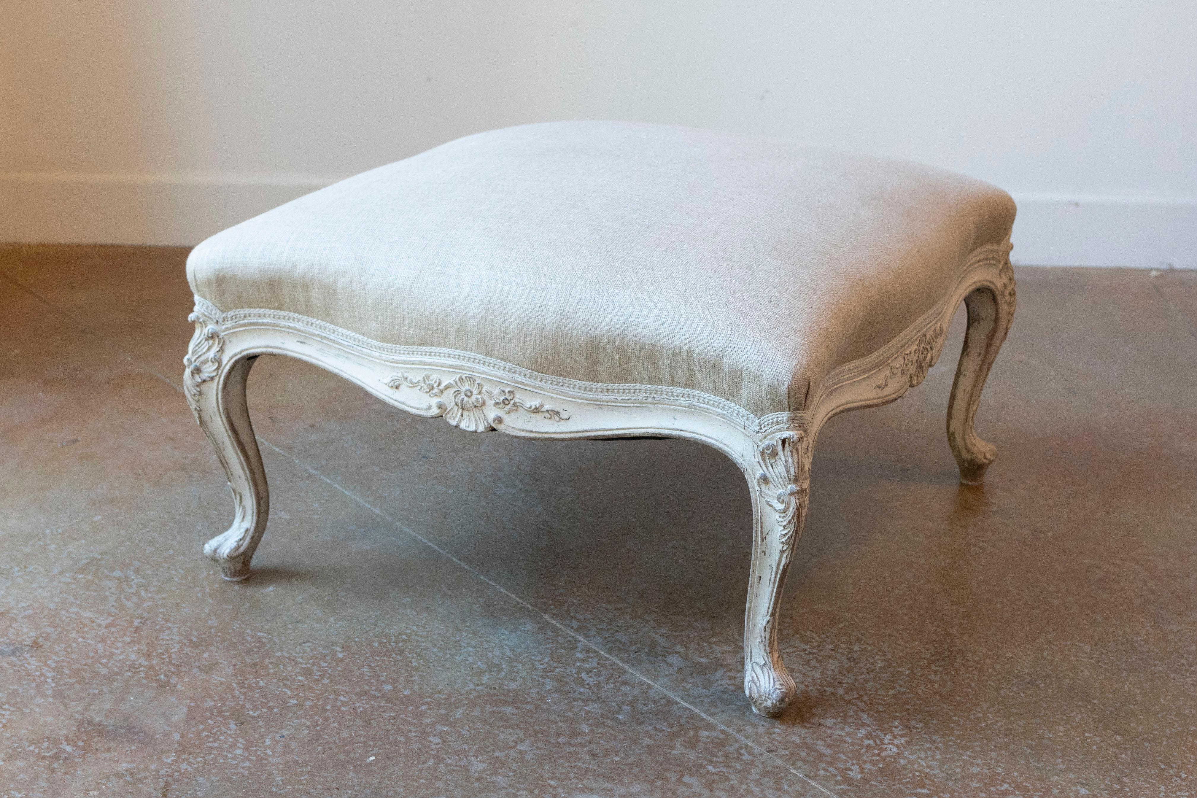 A Swedish Rococo style painted wood stool from the 19th century, with carved shells and newer upholstery. Created in Sweden during the 19th century, this painted stools features a square-shaped seat recovered with a neutral toned fabric, sitting